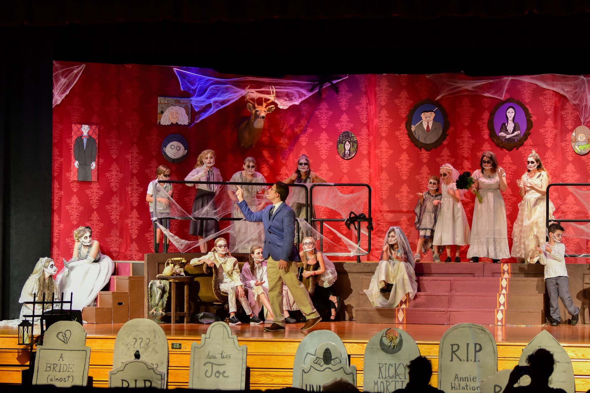 A stage with actors in Halloween costumes. A man in a sweater gestures to the audience.