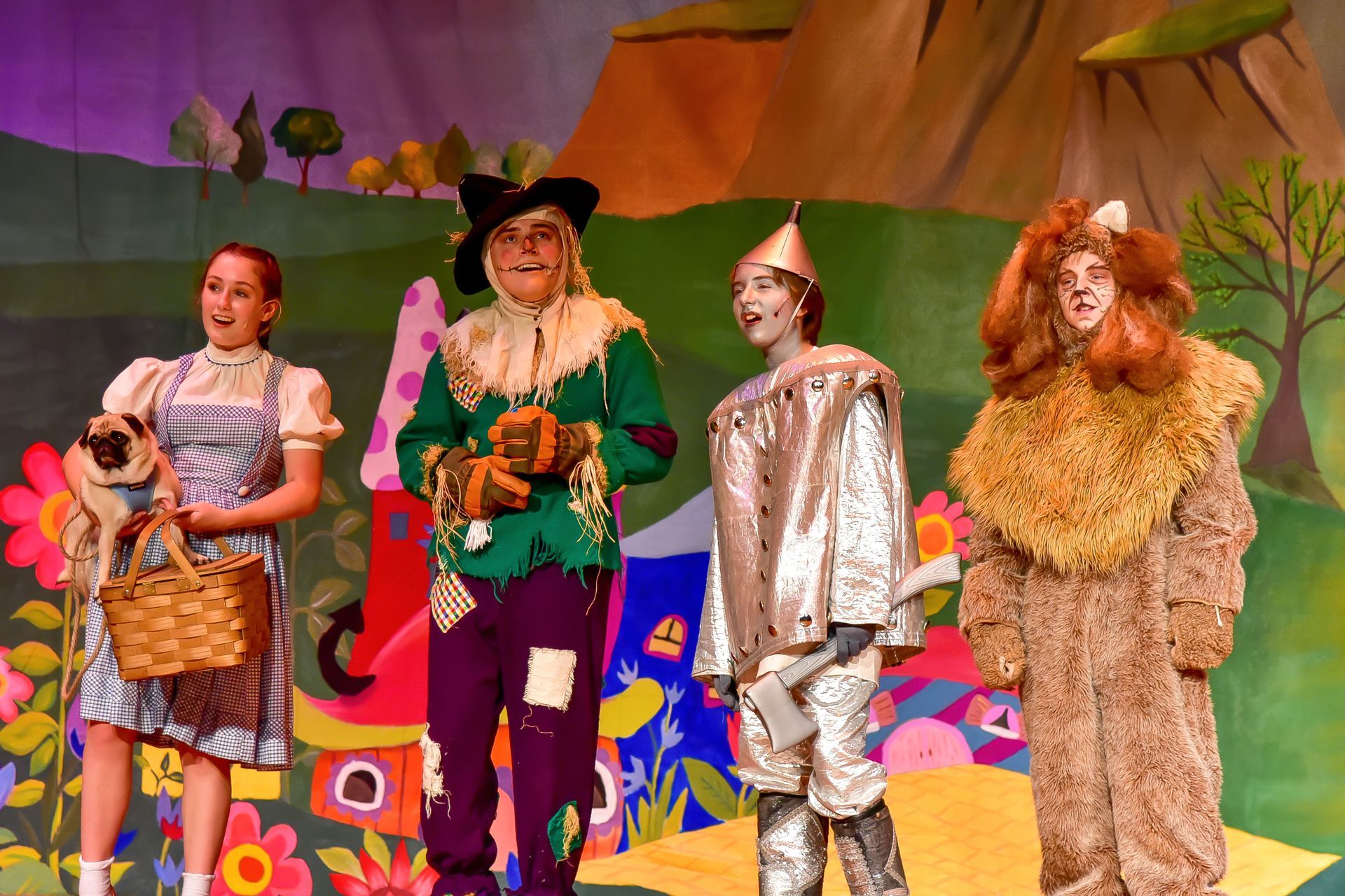 A stage production of The Wizard of Oz with Dorothy, Scarecrow, Tin Man, and Cowardly Lion.