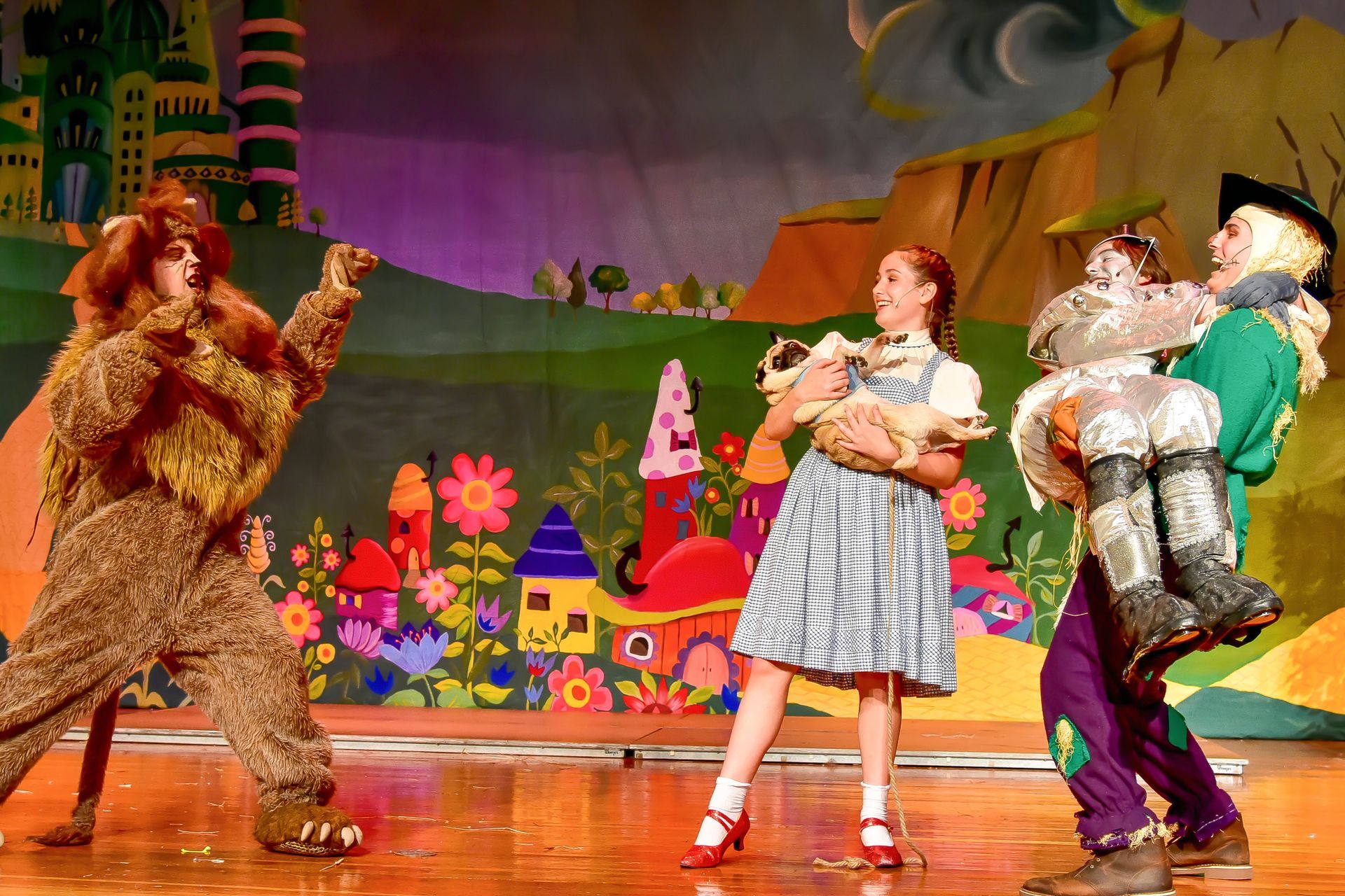 A stage production of The Wizard of Oz with Dorothy, Scarecrow, Tin Man, and Cowardly Lion.