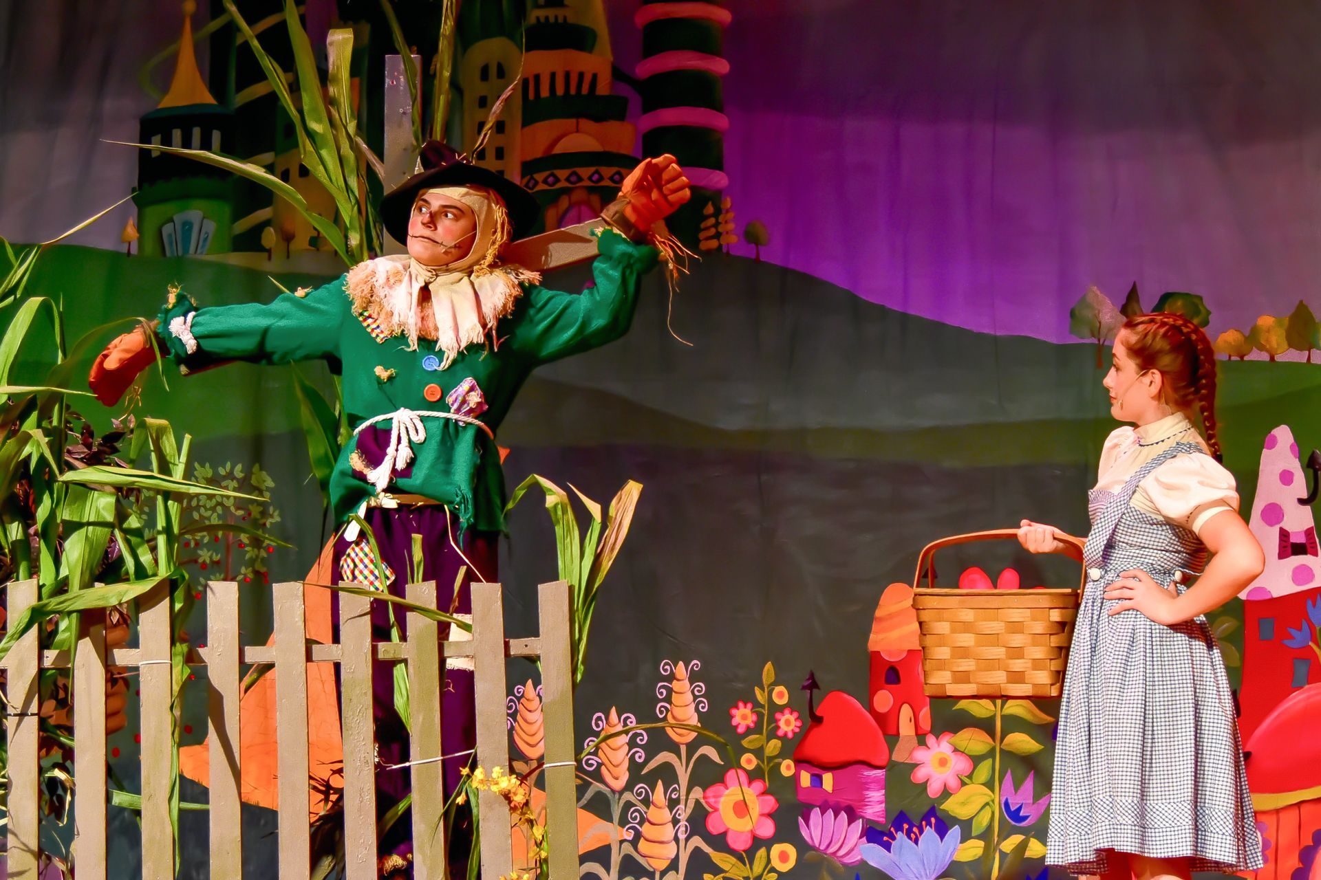 Scarecrow with arms up and Dorothy, in blue dress, looking at him on a Wizard of Oz stage.