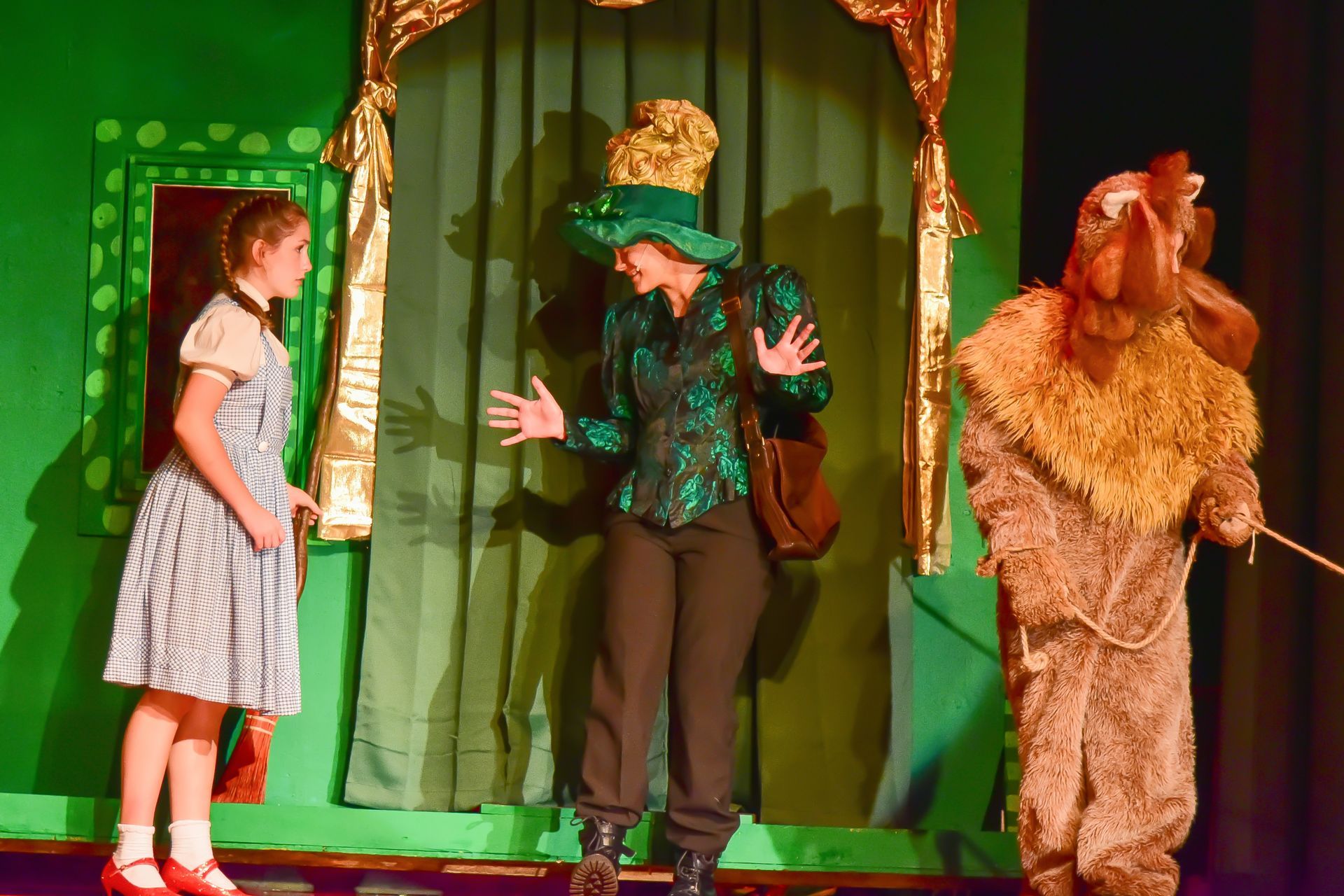 Dorothy, the Wicked Witch, and the Cowardly Lion on a green stage in a Wizard of Oz production.