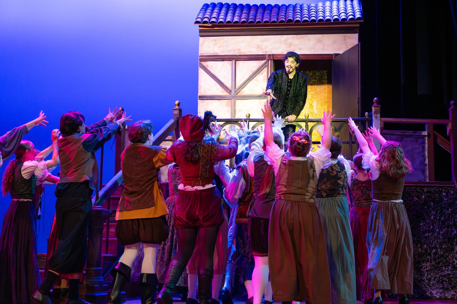 Actors in period costumes perform a musical scene with someone on a balcony. Stage set.