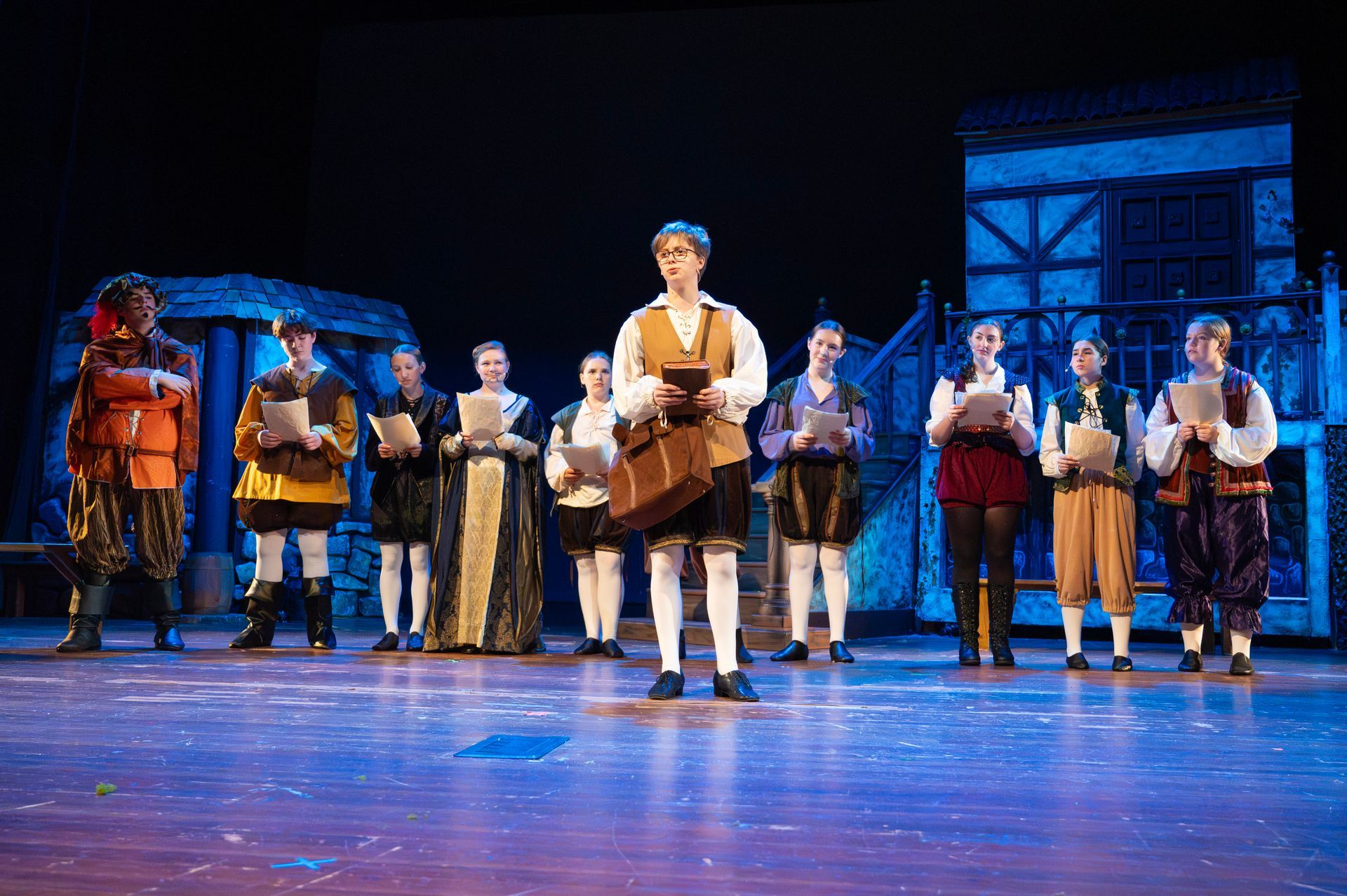 A costumed theatrical performance. A group of people on stage are holding scripts.