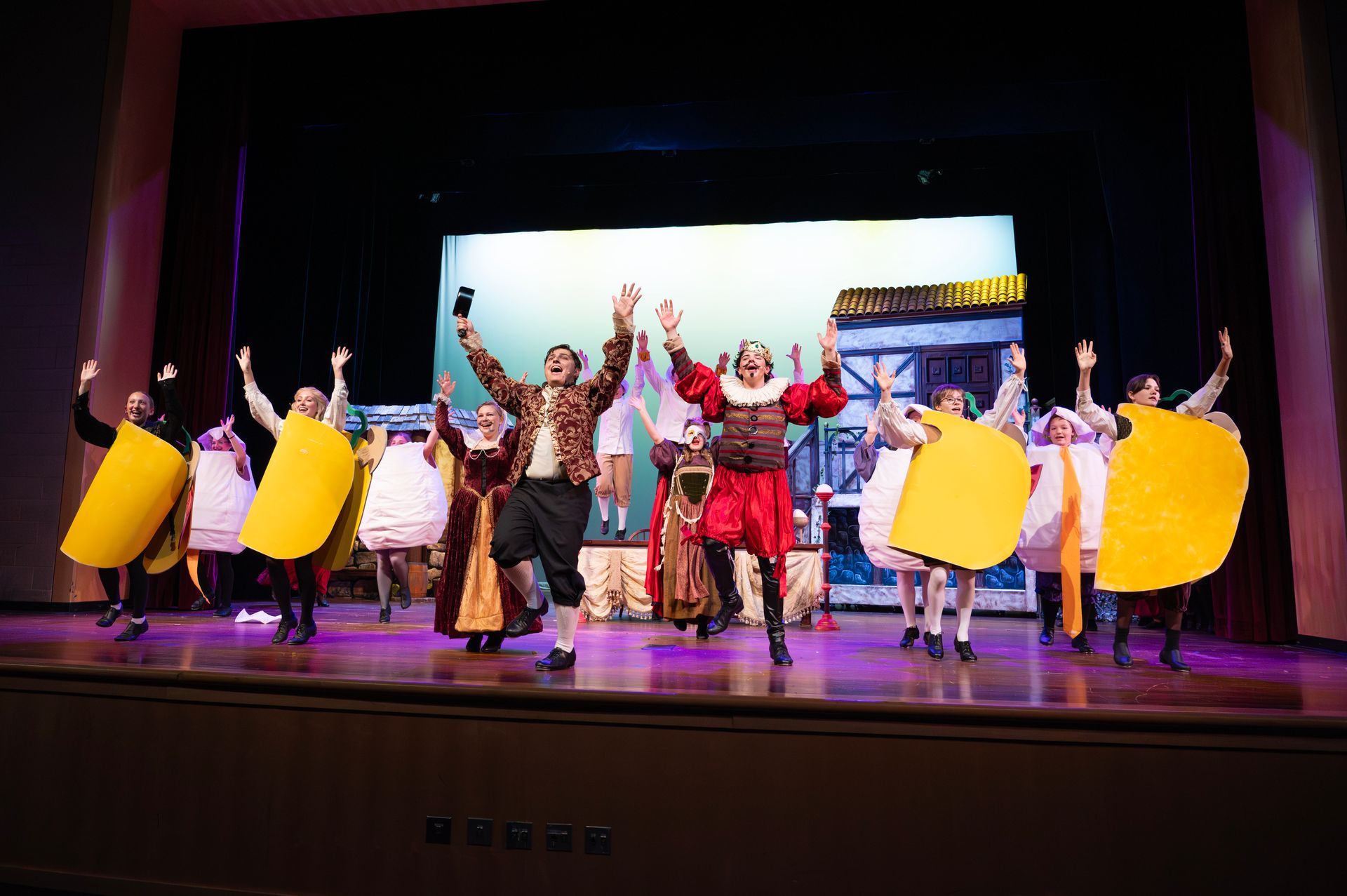 A theater stage with actors in costumes. Some wear large yellow taco costumes, others wear period clothing.