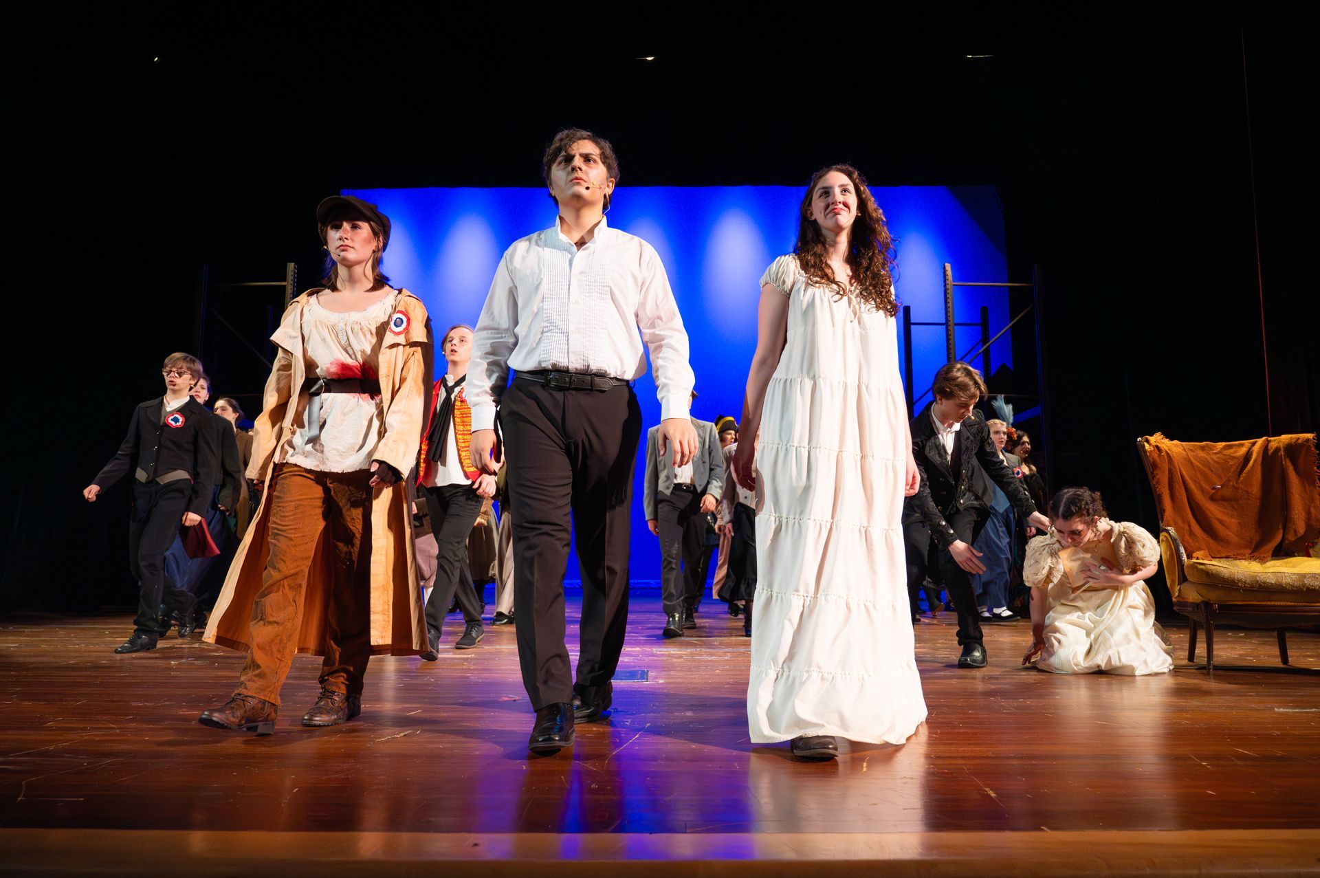 A theatrical stage with actors, two in front, others behind. Blue backdrop, wood floor.