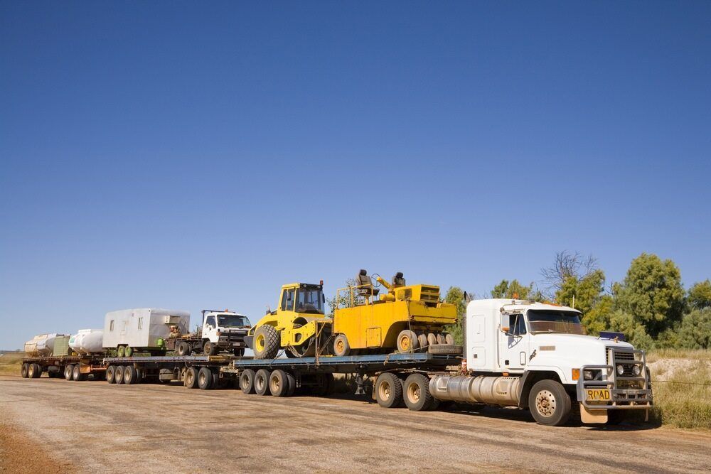 A Row Of Semi Trucks Are Driving Down A Dirt Road — Geisler Truck & Trailer Wheel Alignments In Marian, QLD