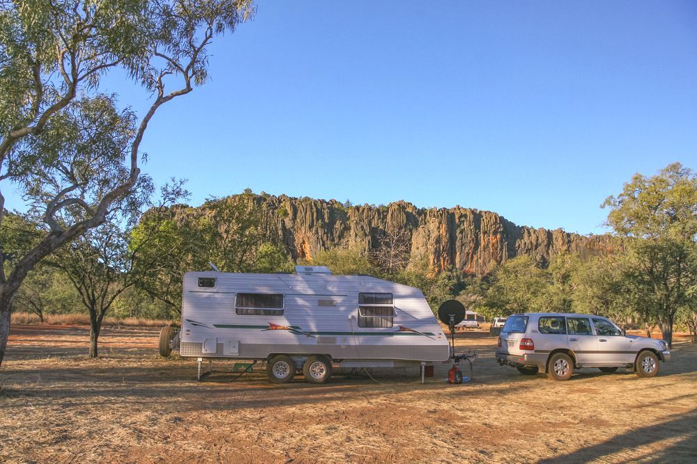 A Caravan Is Parked In A Dirt Field With A Mountain — Geisler Truck & Trailer Wheel Alignments In Marian, QLD