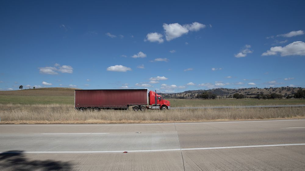 A Red Semi Truck Is Driving Down A Highway Next To A Field — Geisler Truck & Trailer Wheel Alignments In Pleystowe, QLD