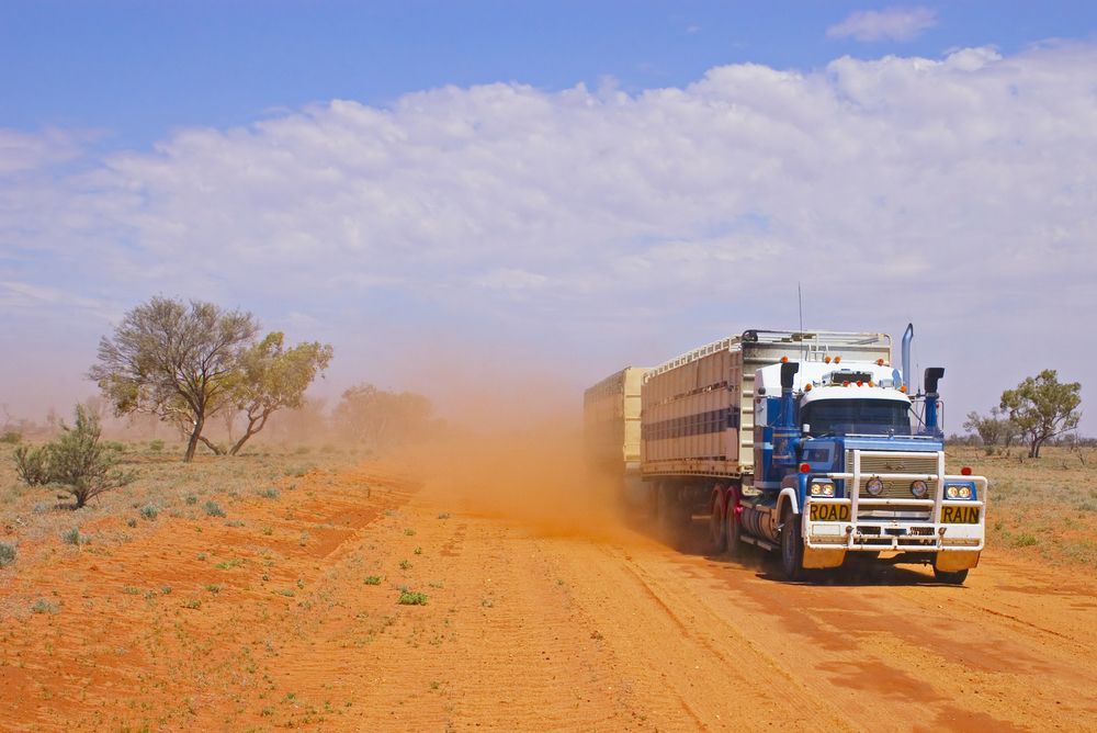 A Semi Truck Is Driving Down A Dirt Road In The Desert — Geisler Truck & Trailer Wheel Alignments In Mackay, QLD