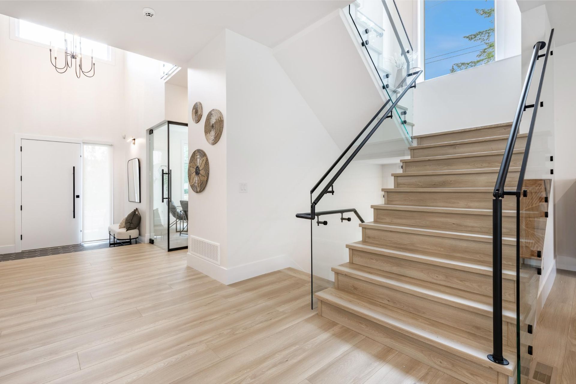 Spacious white foyer with wooden staircase, glass railing, and double doors.