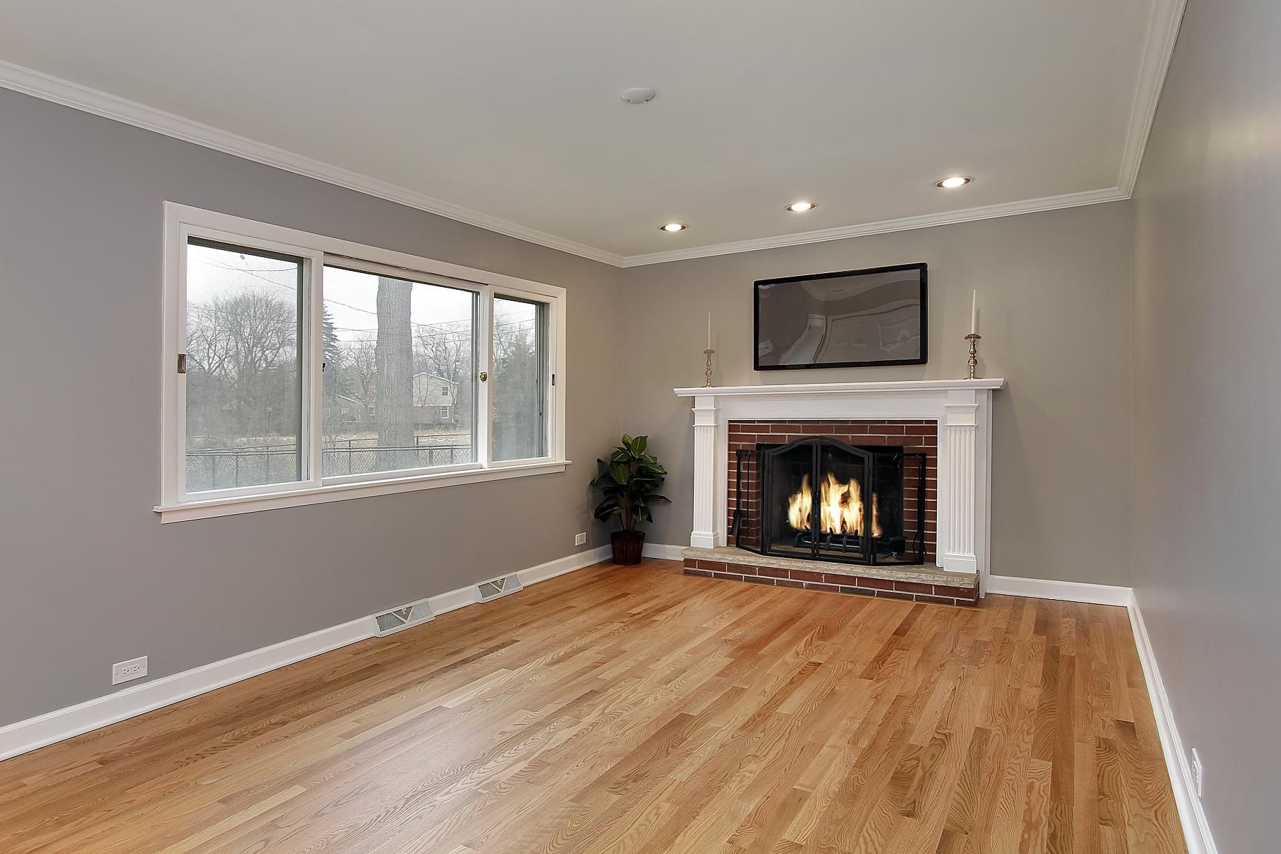 Empty living room with fireplace, window, hardwood floor, gray walls.