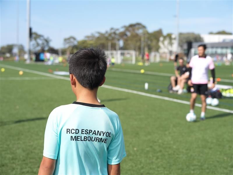 A boy wearing a shirt that says Rcd Espanyol Melbourne stands on a soccer field