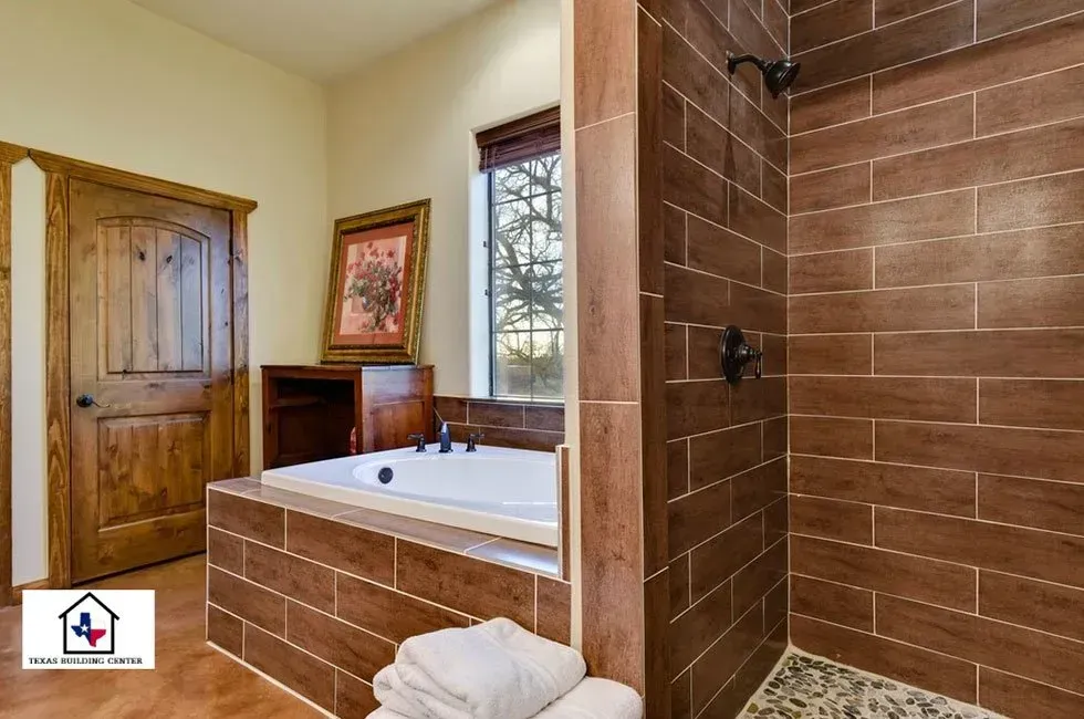 Bathroom with brown wood-look tile, soaking tub, walk-in shower, wooden door, and small window.