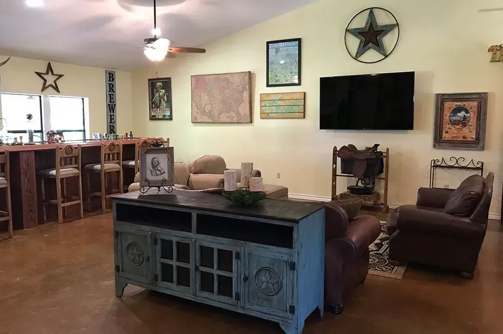 Living room with bar and rustic decor, including a blue cabinet, brown leather chairs, and star-shaped artwork.