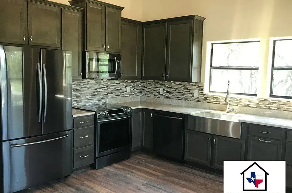 Dark gray kitchen with stainless steel appliances, backsplash, and farmhouse sink.