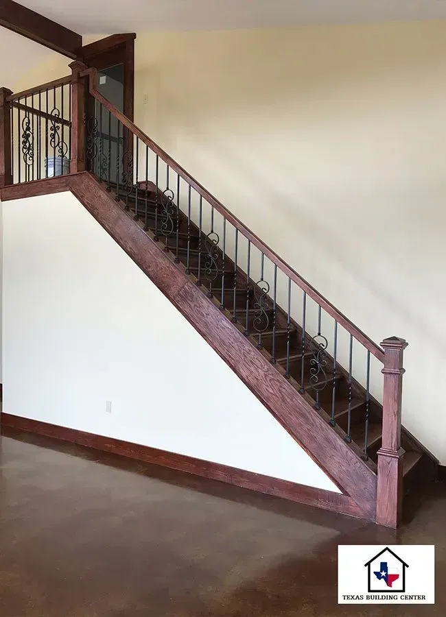 Staircase with dark wood, black wrought iron railing. Brown concrete floor, beige walls.