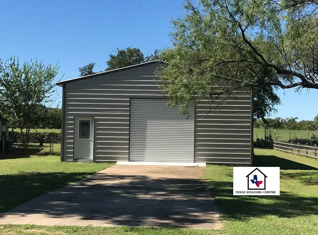 Metal garage with a roll-up door and a small door on a concrete pad, under a blue sky.