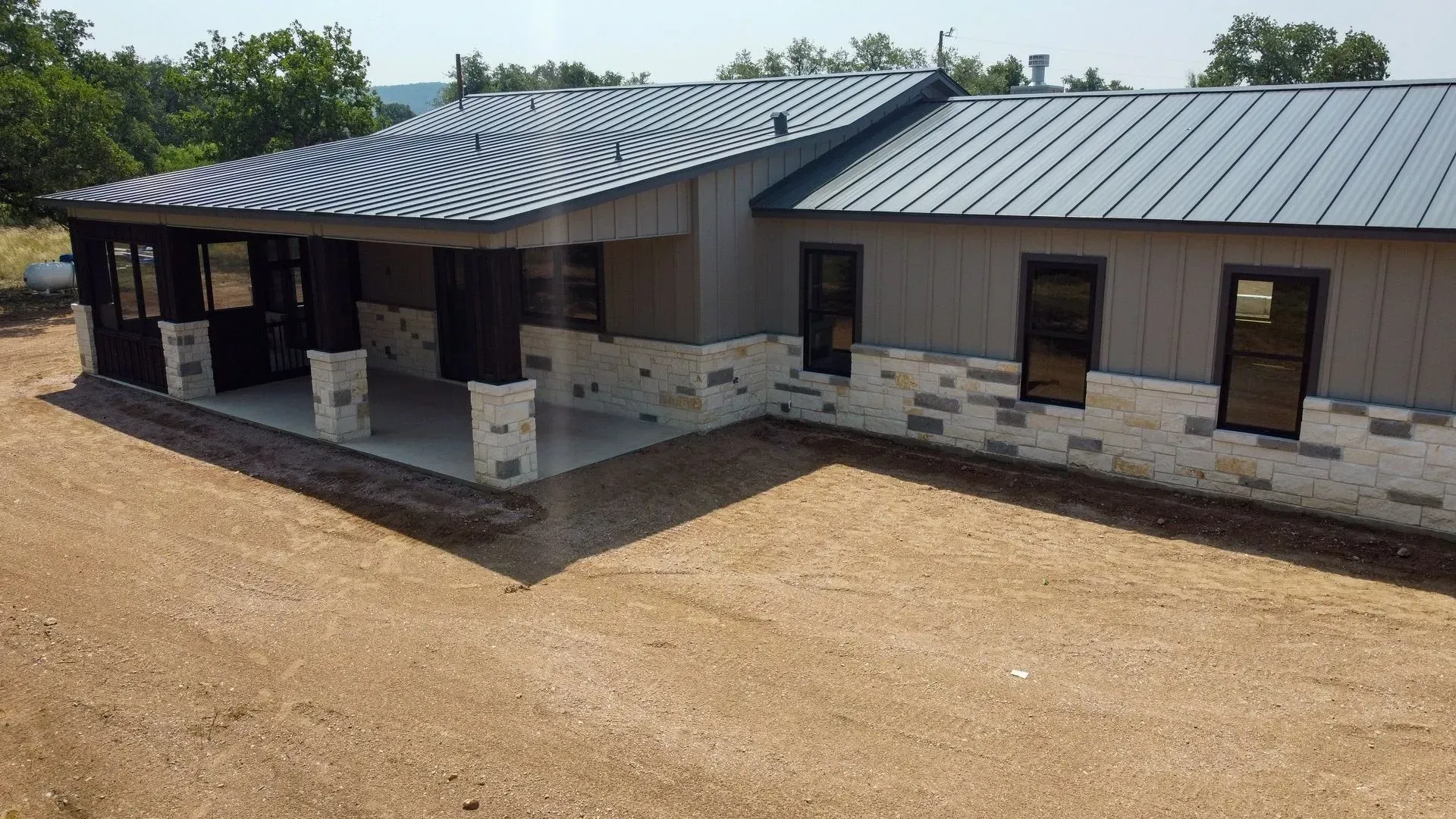 Modern house with gray metal roof, porch, stone accents, and windows on gravel driveway.
