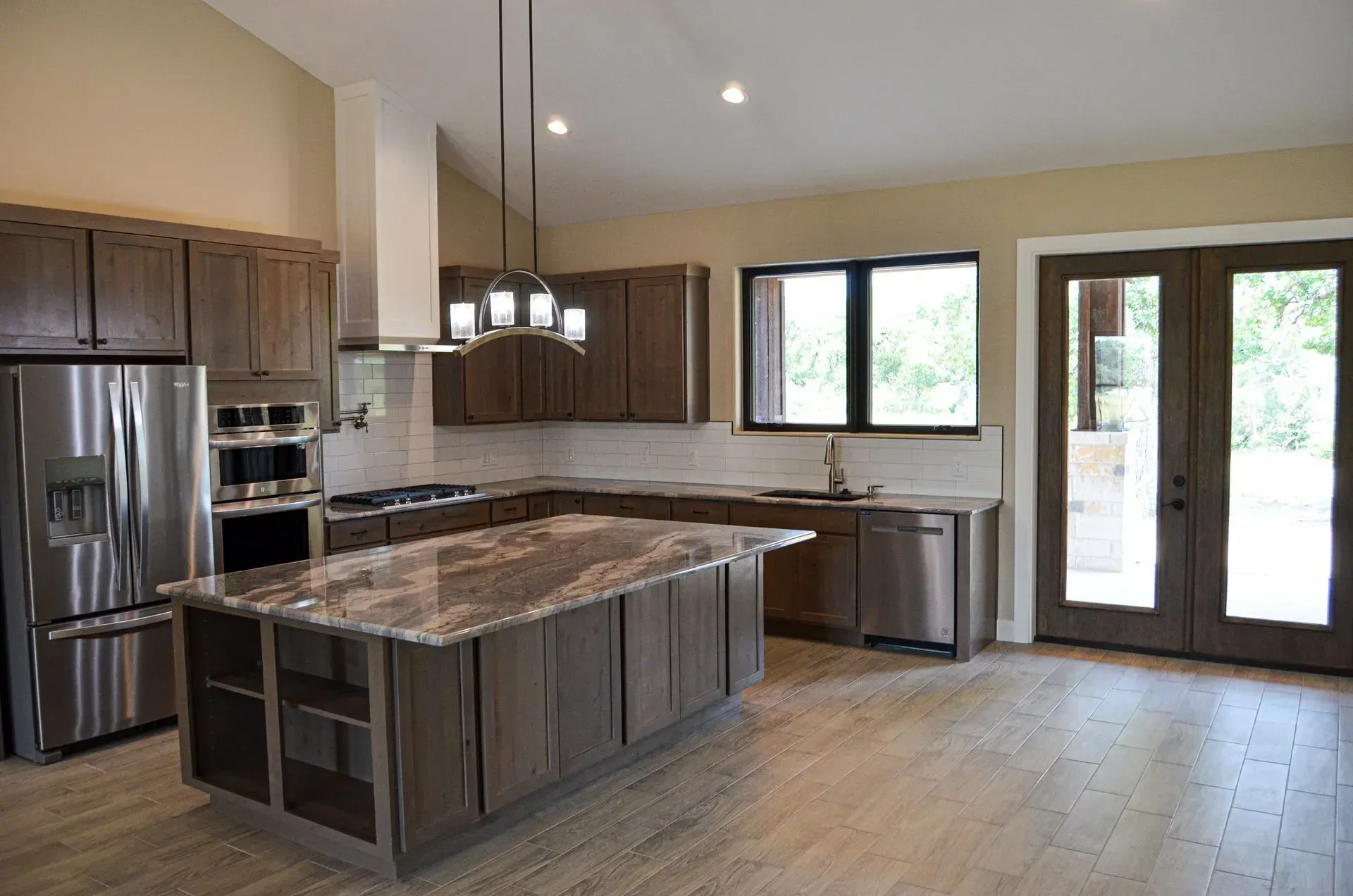 Modern kitchen with stainless steel appliances, brown cabinets, and a large island.