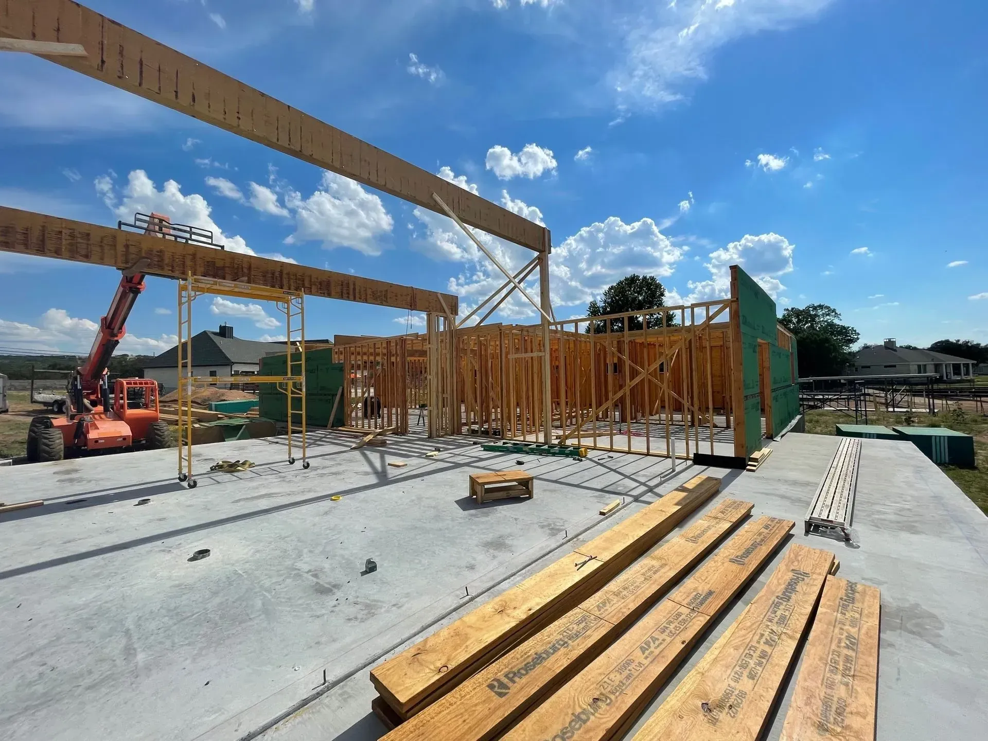 Construction site: wooden frame building under construction with lumber, orange lift, blue sky.
