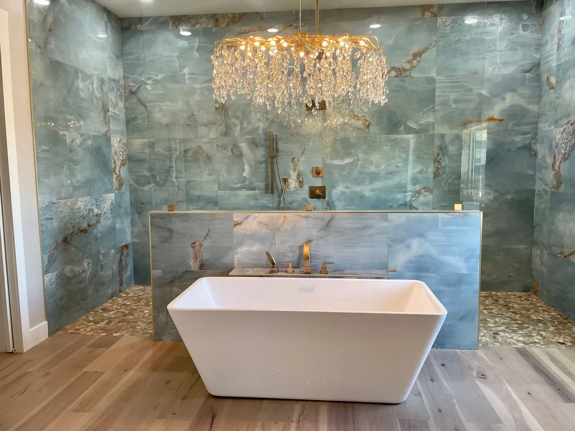 Luxurious bathroom with blue tile, a white tub, and a crystal chandelier.