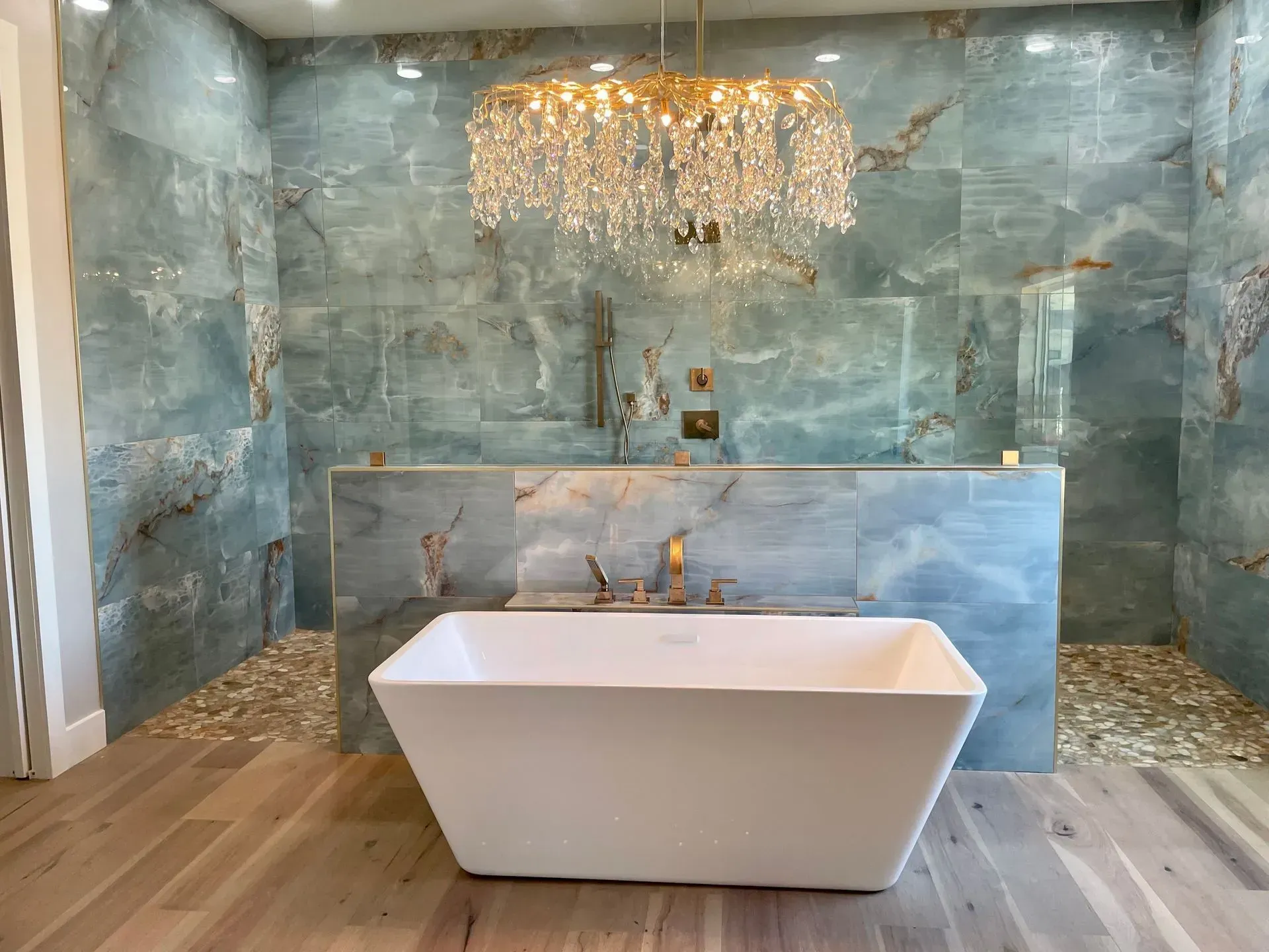 Luxurious bathroom with a blue stone wall, a white tub, and a crystal chandelier.