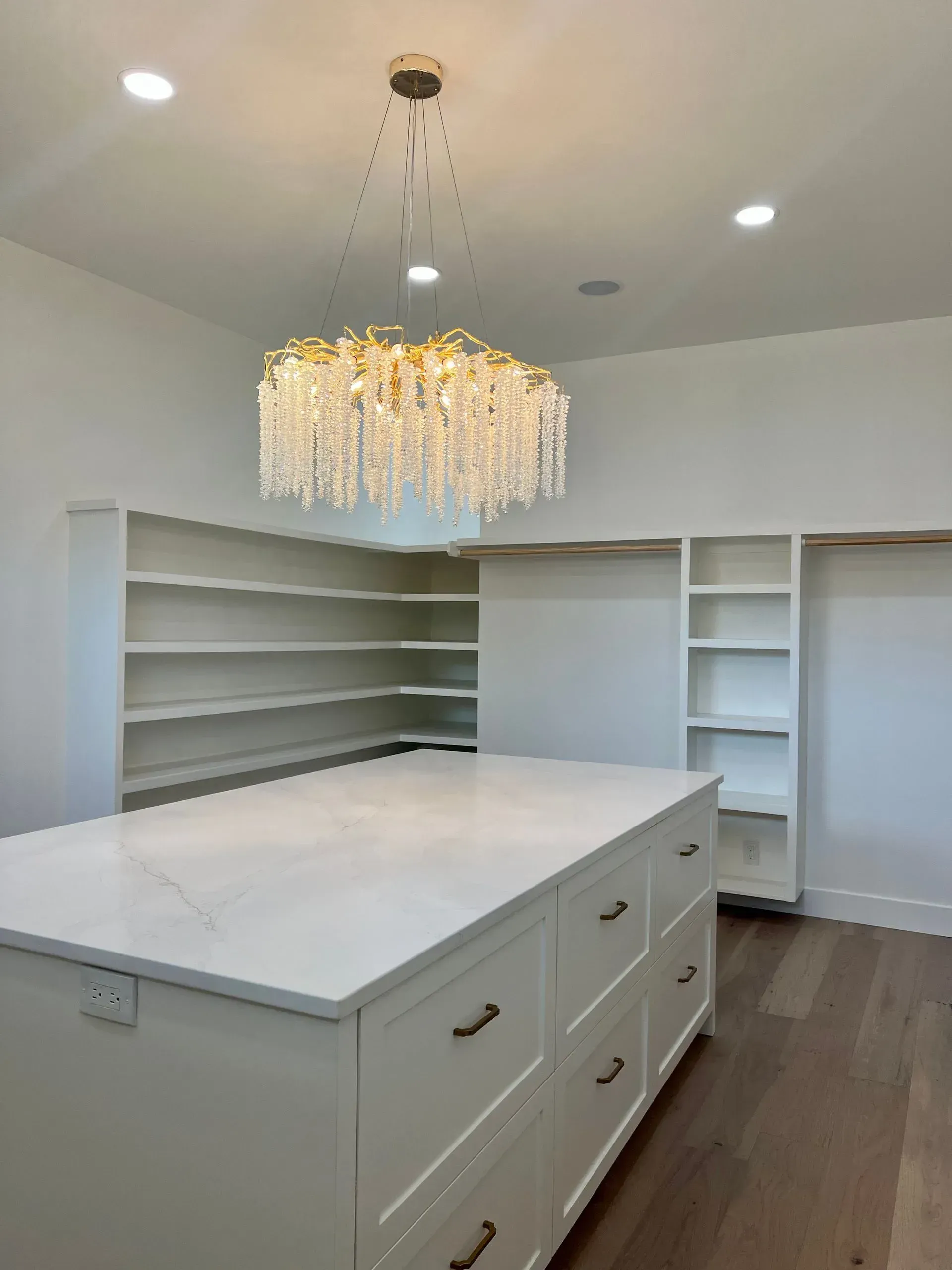 A white closet island with drawers under a gold chandelier in a bright room.