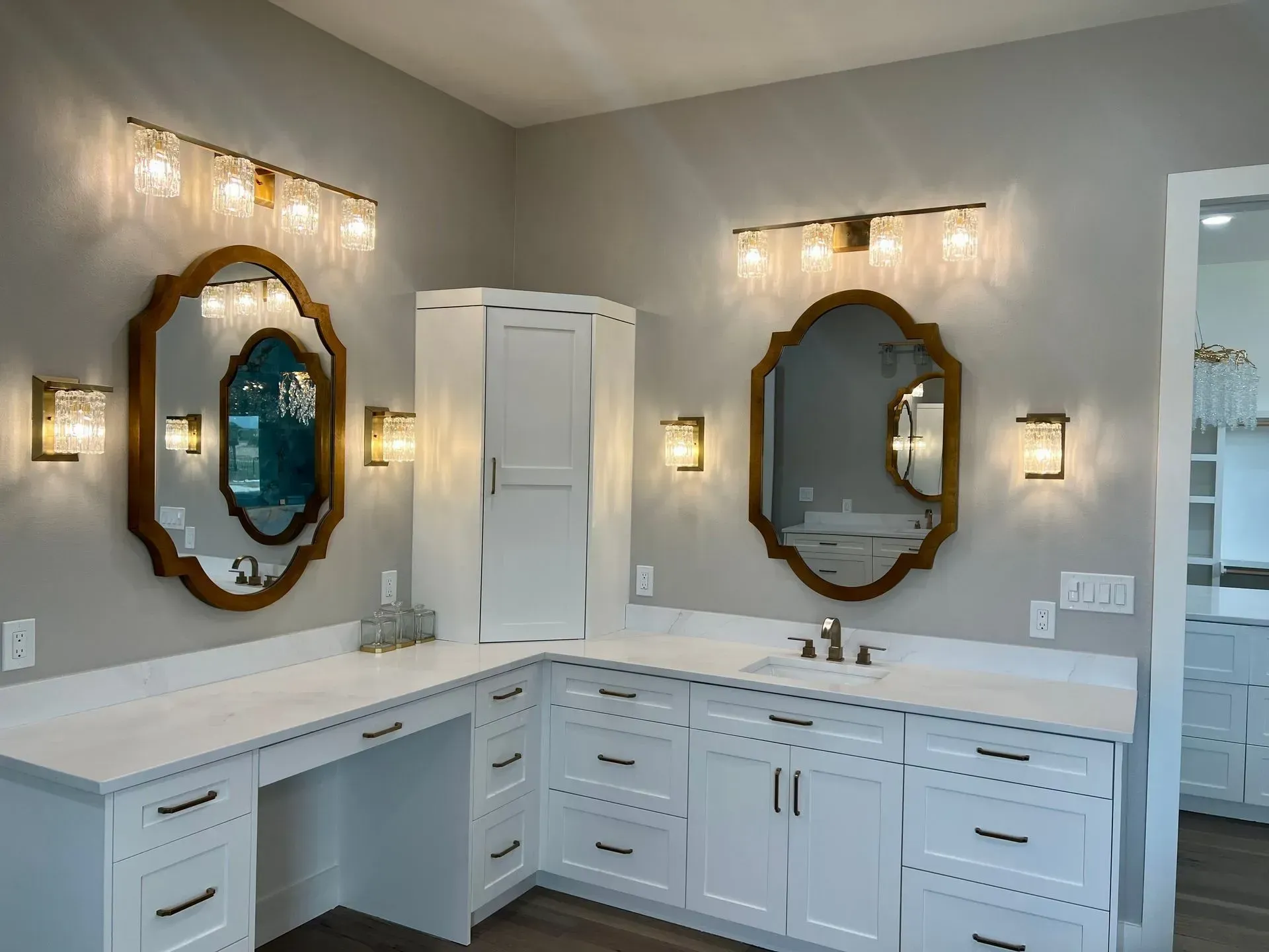 Bathroom with white cabinets, two gold-framed mirrors, and sconces. Gray walls, white countertop.