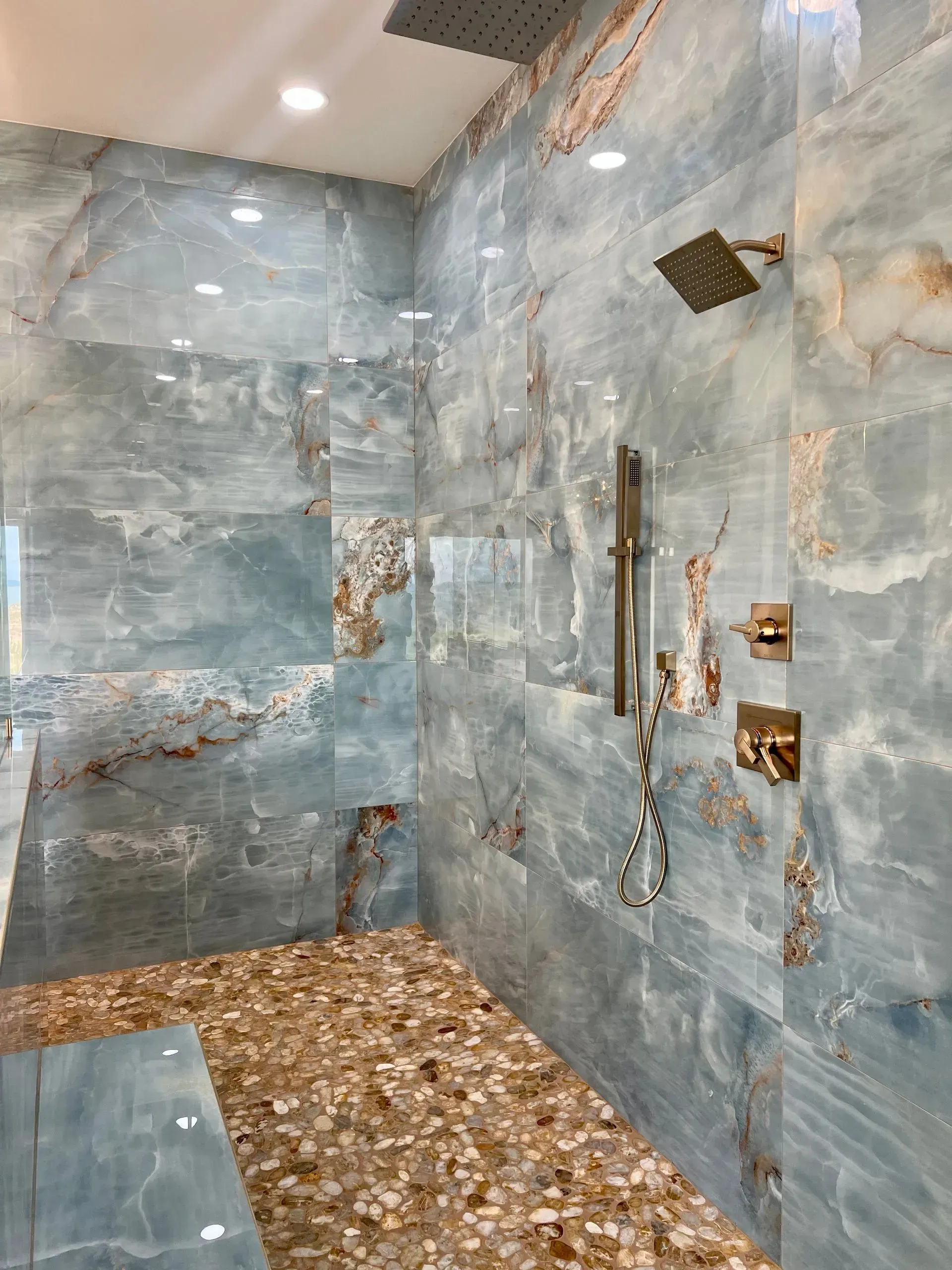 Blue and brown tiled shower with pebble floor and gold fixtures.