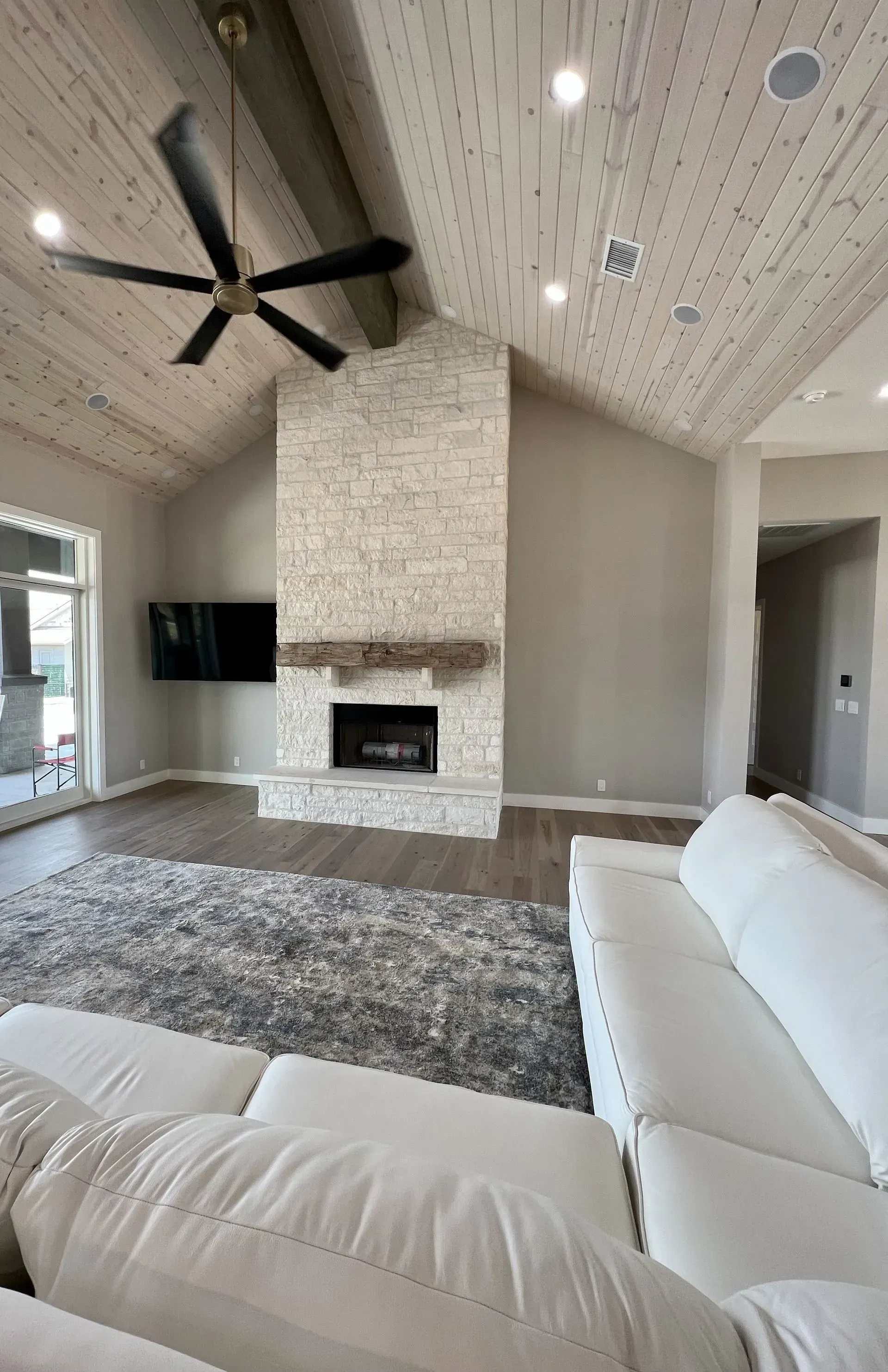 Living room with vaulted, textured ceiling, stone fireplace, TV, gray rug, and white sofa.