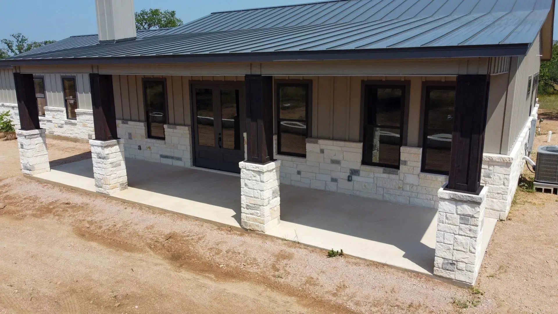A covered porch with stone columns and a gray metal roof on a new house.