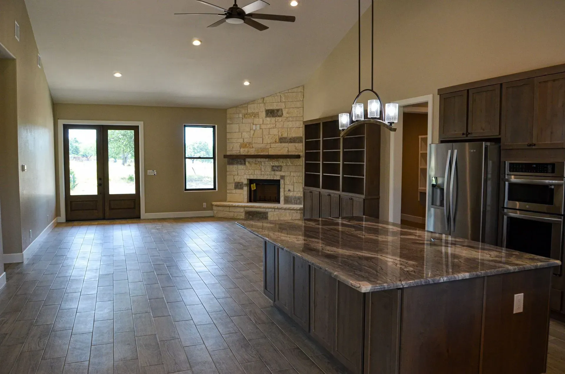 Open concept kitchen and living area with stone fireplace, dark wood cabinets, and a large island.
