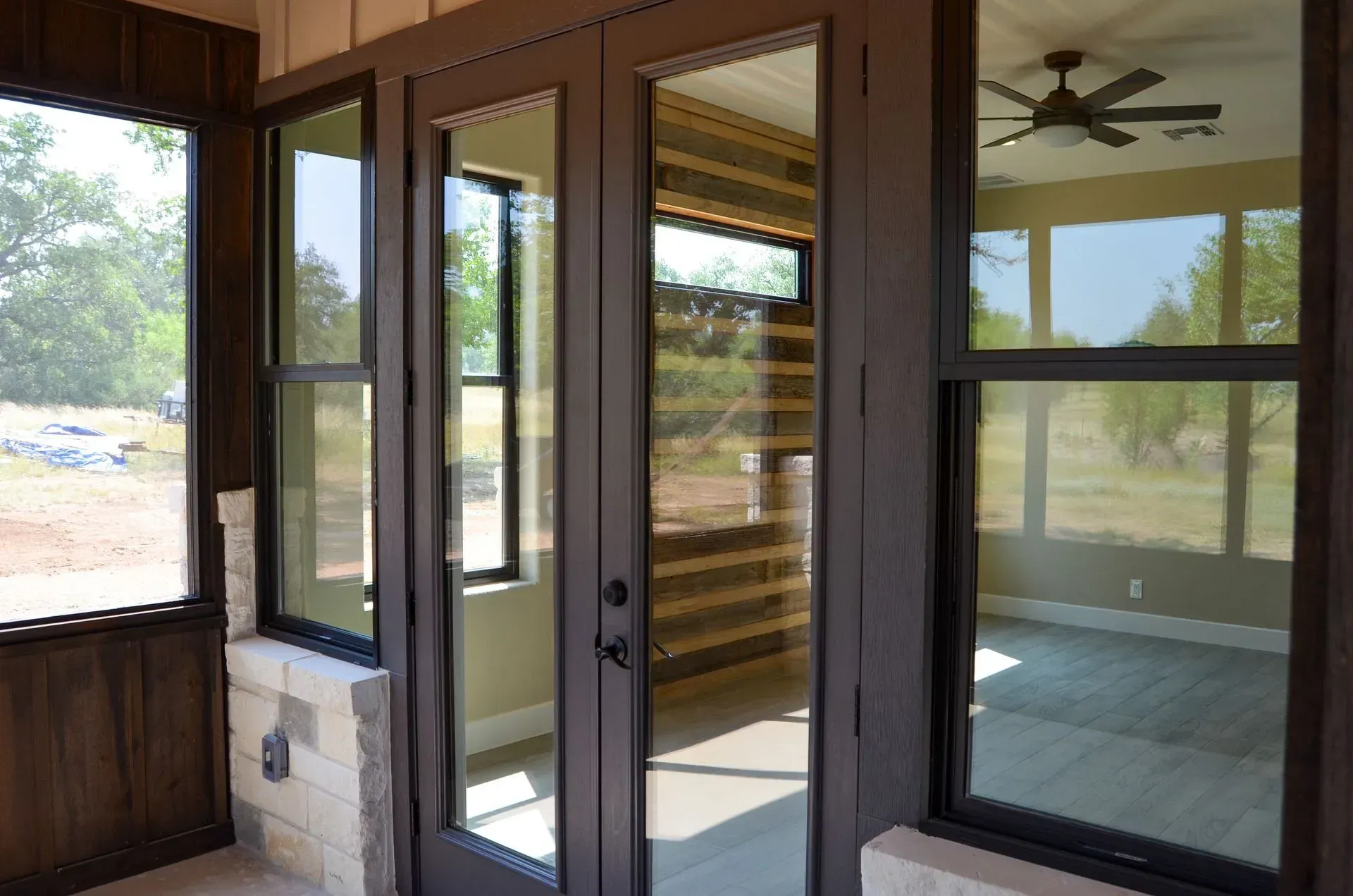 Brown framed glass doors and windows on a porch, looking into a modern home.