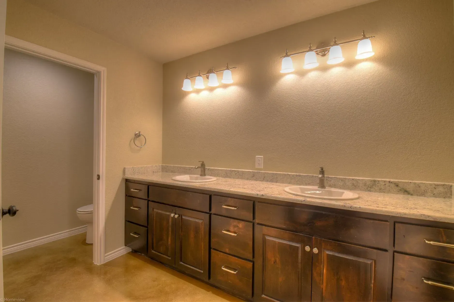 Bathroom with dark wood cabinets, dual sinks, granite countertop, and two light fixtures.