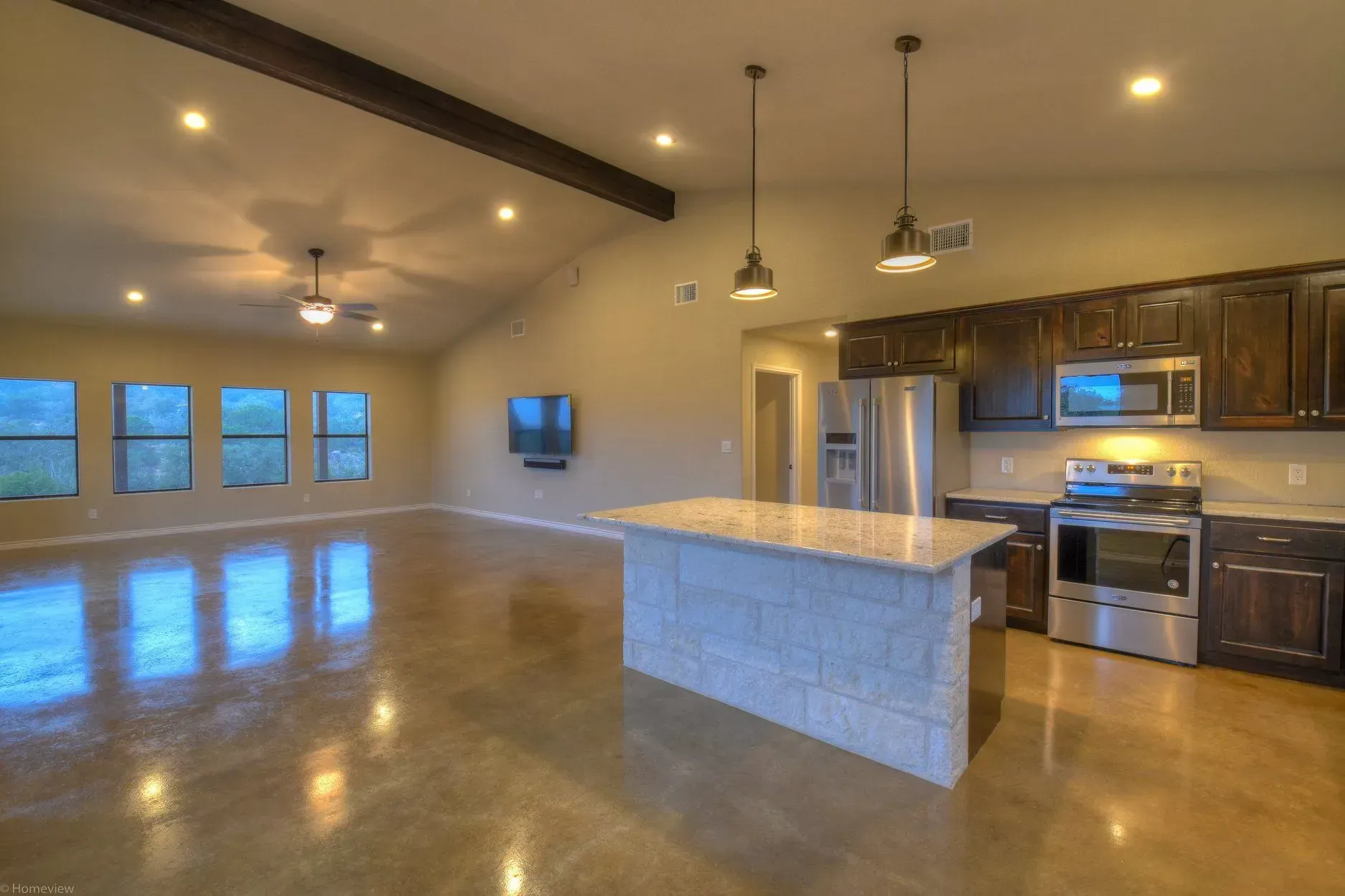 Modern kitchen with island, stainless steel appliances, dark cabinets, and open living space.
