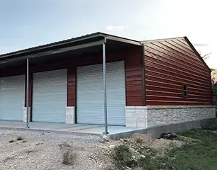 Red metal building with three garage doors, stone base, and a covered porch.
