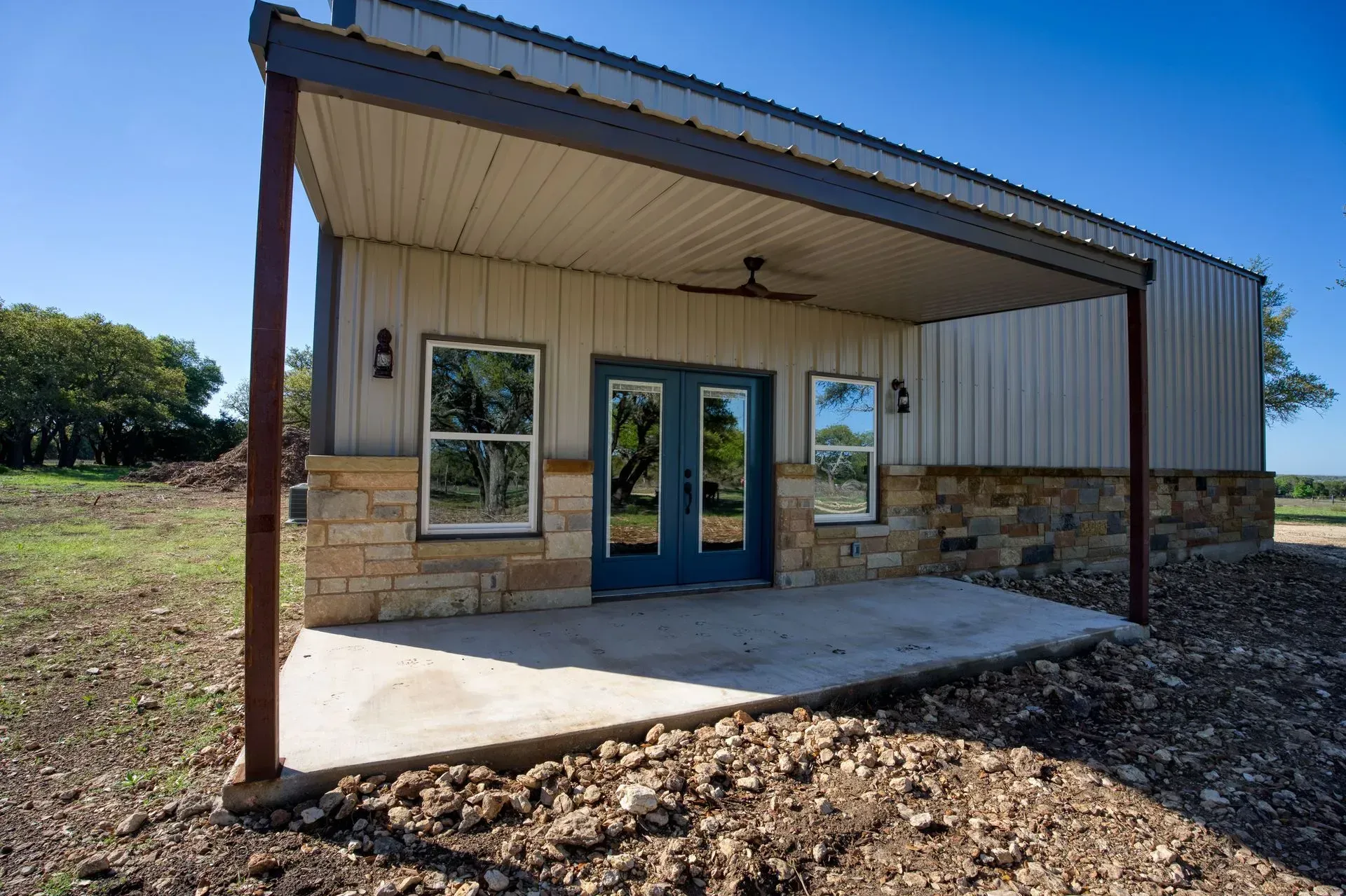 Metal building with stone accents, blue doors, and a covered porch, on a sunny day.