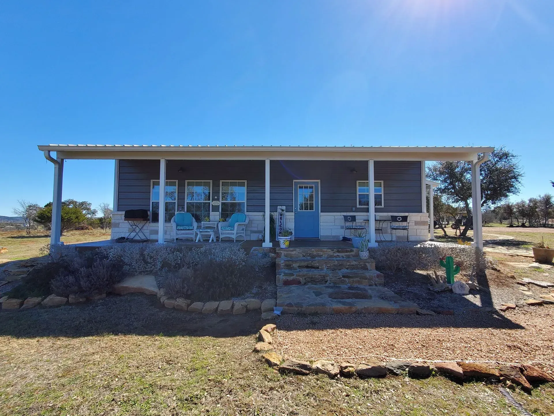 A small, gray house with a blue door, white porch, and a blue sky.