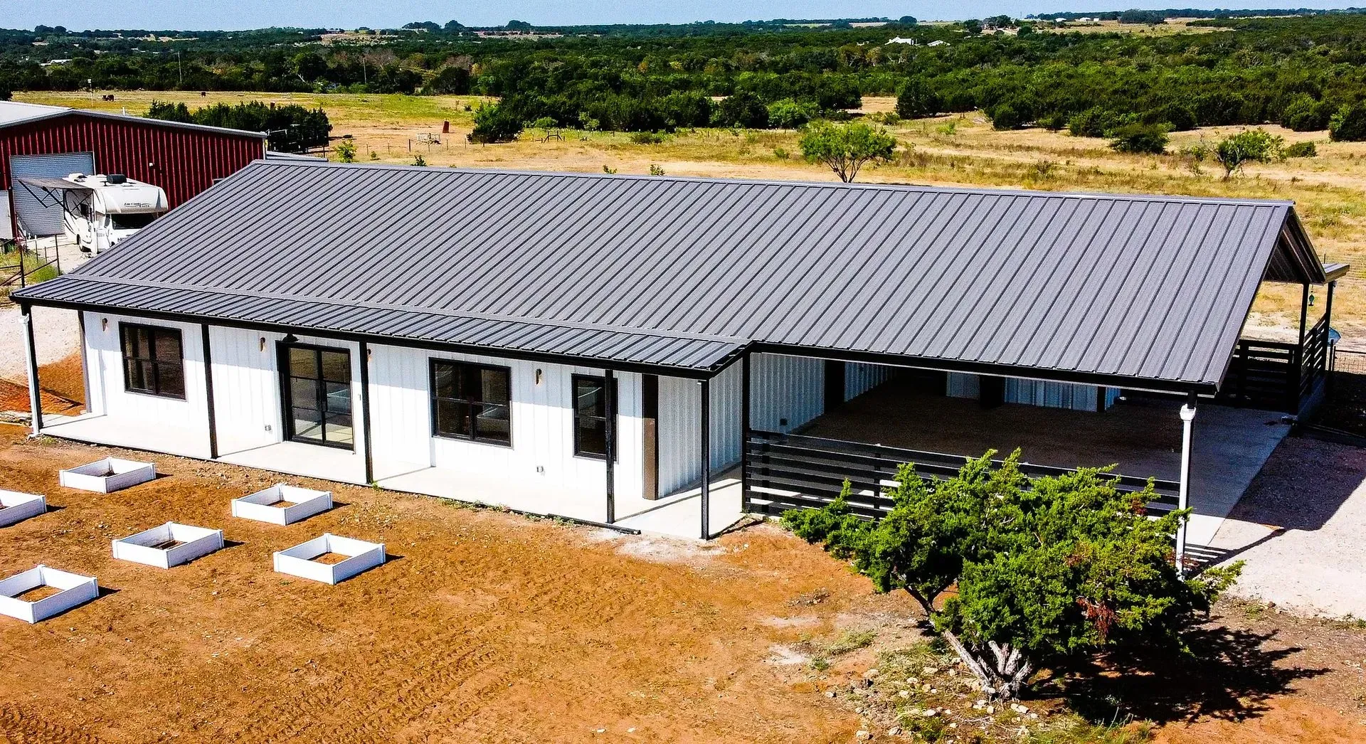 White ranch-style house with gray roof, outdoor deck, and surrounding farmland.