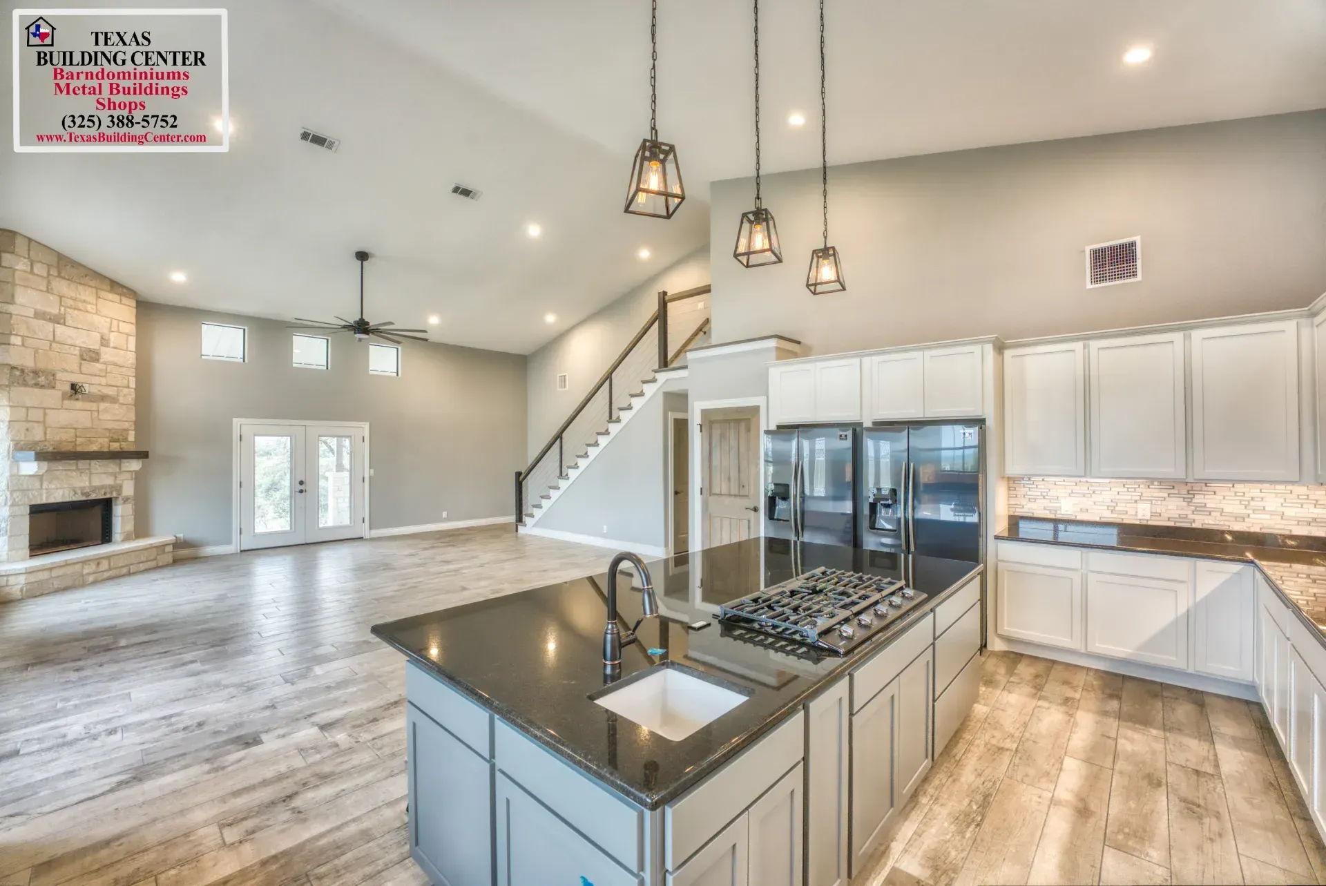 Spacious, open-concept kitchen with island, stainless steel appliances, and stone fireplace in a modern home.