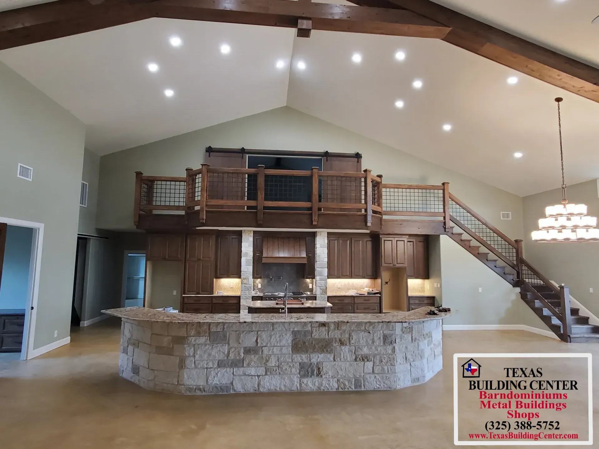 Spacious kitchen with stone island, wooden cabinets, balcony, and staircase in a home.