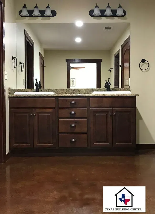 Double sink vanity with dark cabinets, granite countertop, large mirror, and sconce lighting.