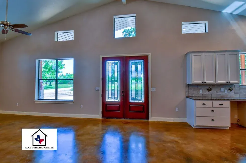 Interior of a house with red double doors and white cabinets, featuring large windows and a vaulted ceiling.