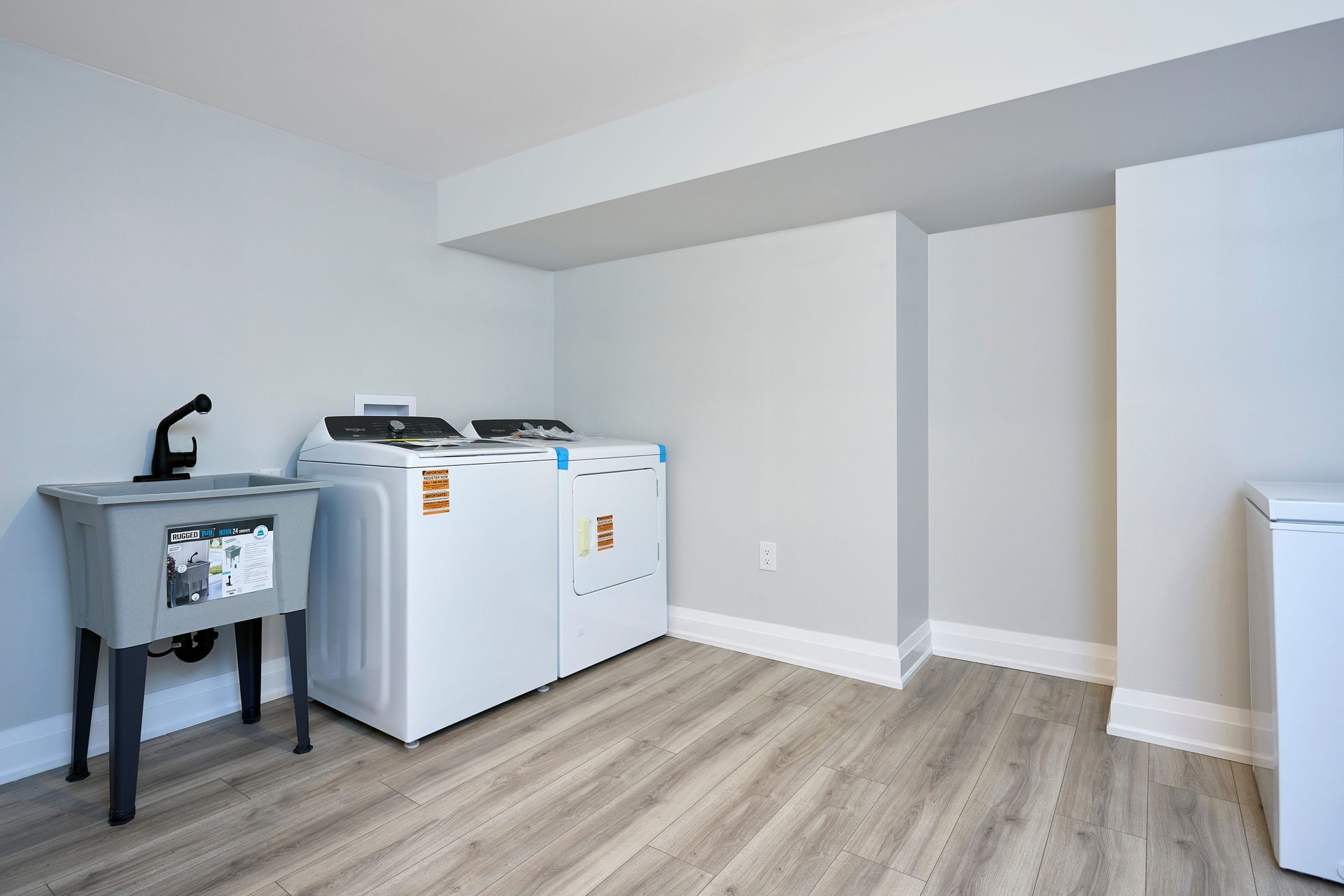 Laundry room with a washing machine, dryer, utility sink, and a freezer on wood-look flooring.