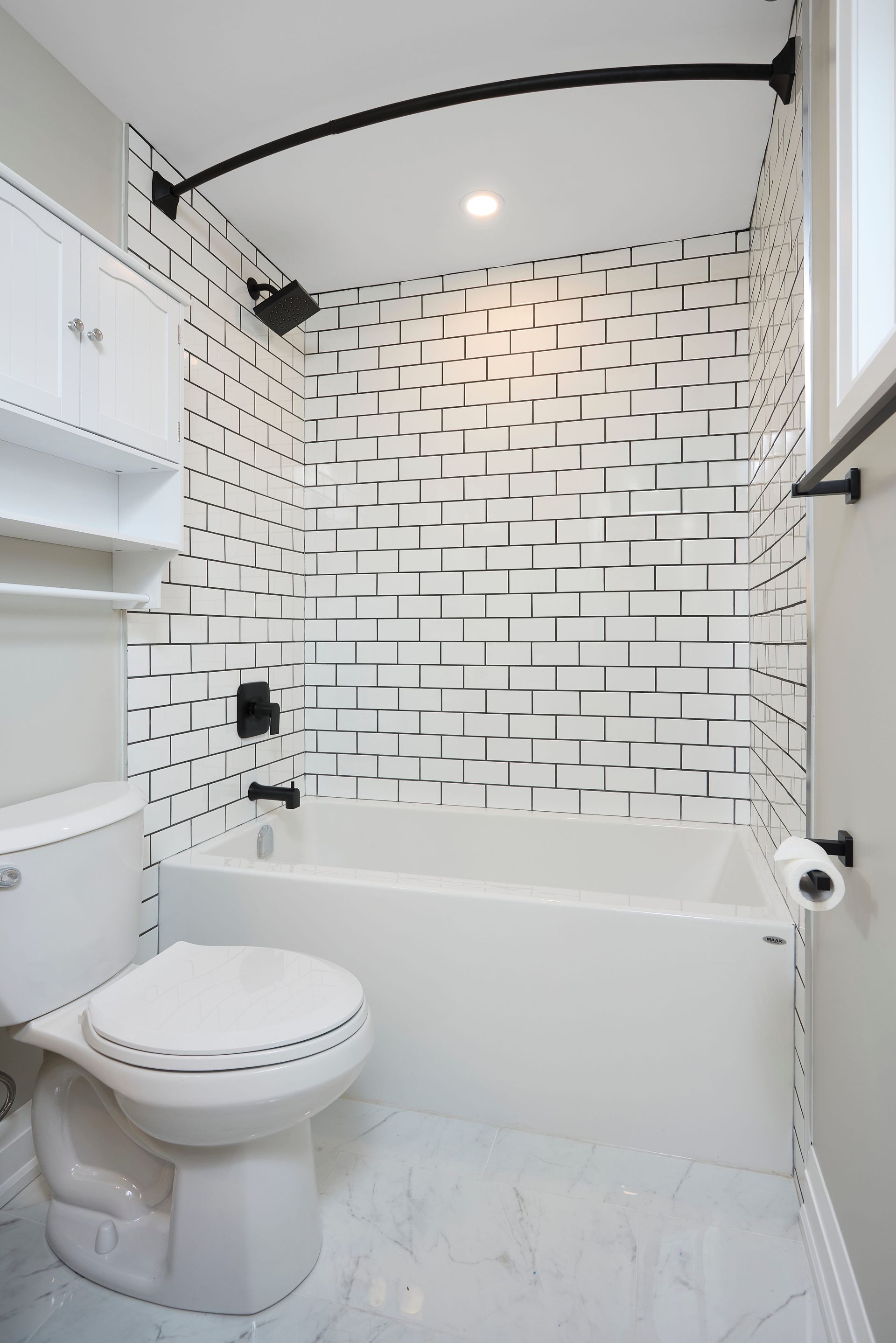 Bathroom with white tiles, black accents, toilet, and shower/tub combo.