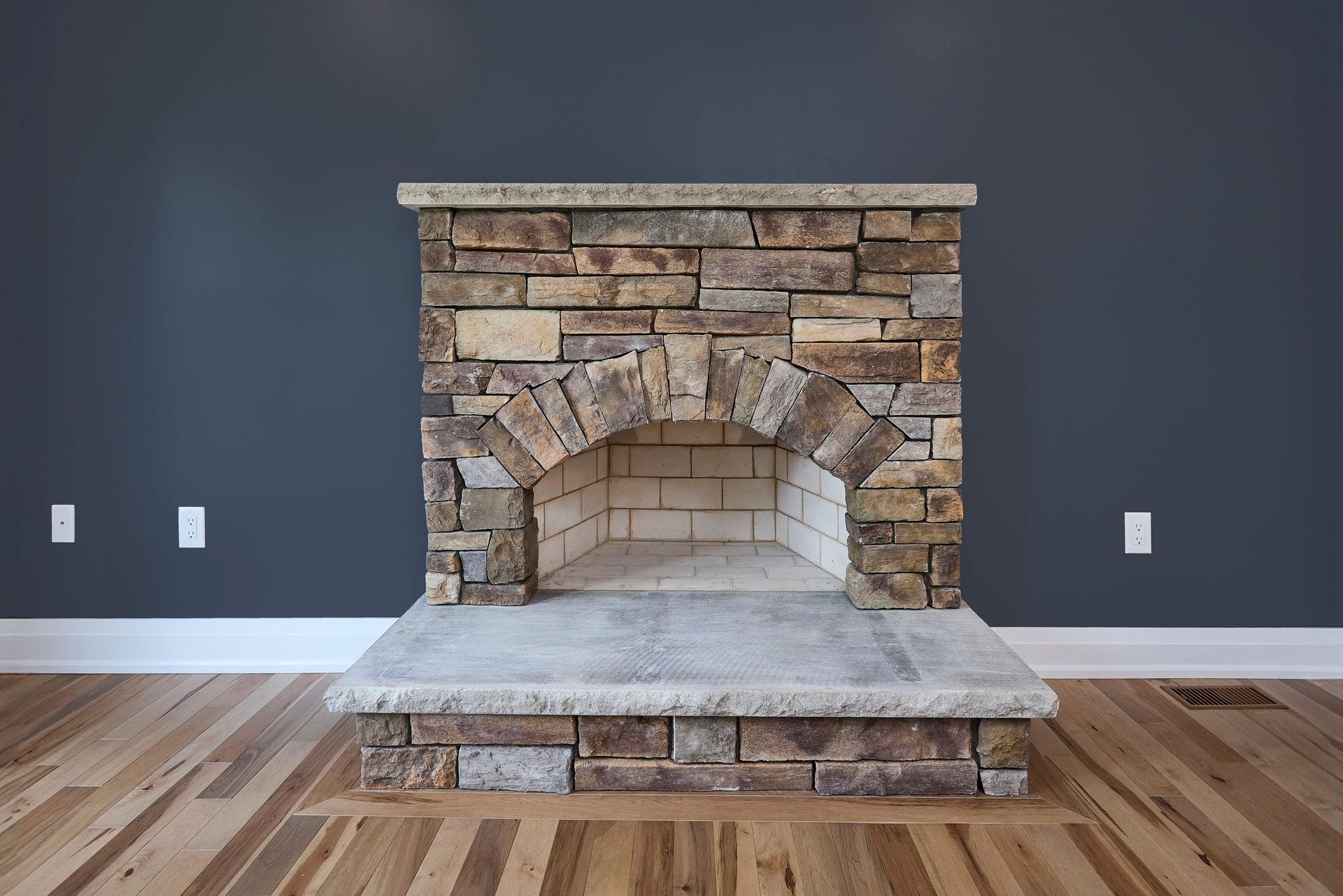 Stone fireplace with an arched opening, against a dark blue wall. Light-colored hardwood floor.