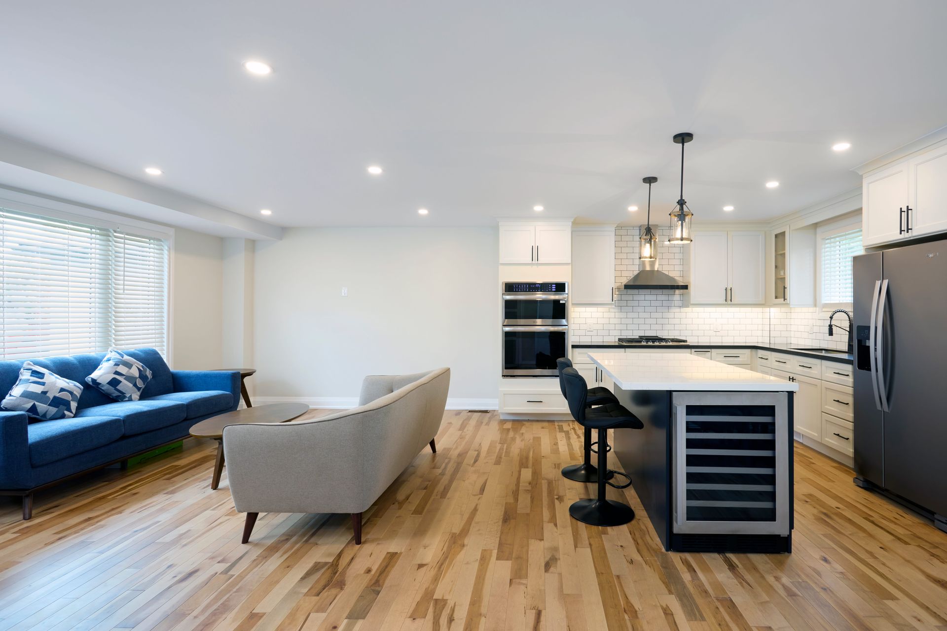 Open-concept living space with a blue sofa, gray sofa, kitchen island with seating, and a stainless steel refrigerator.