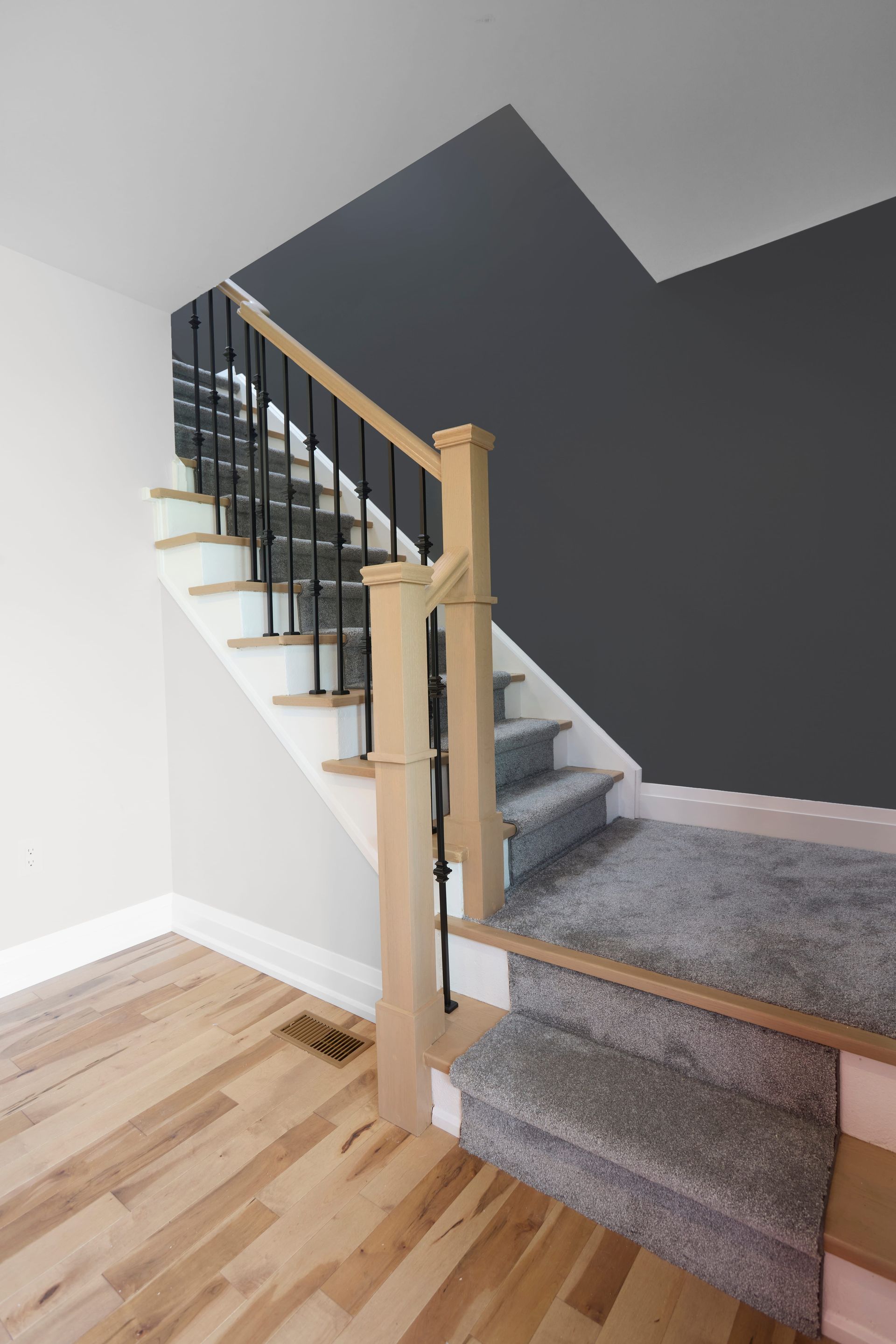 Staircase with light wood flooring, white risers, grey carpeted stairs, and dark grey accent wall.