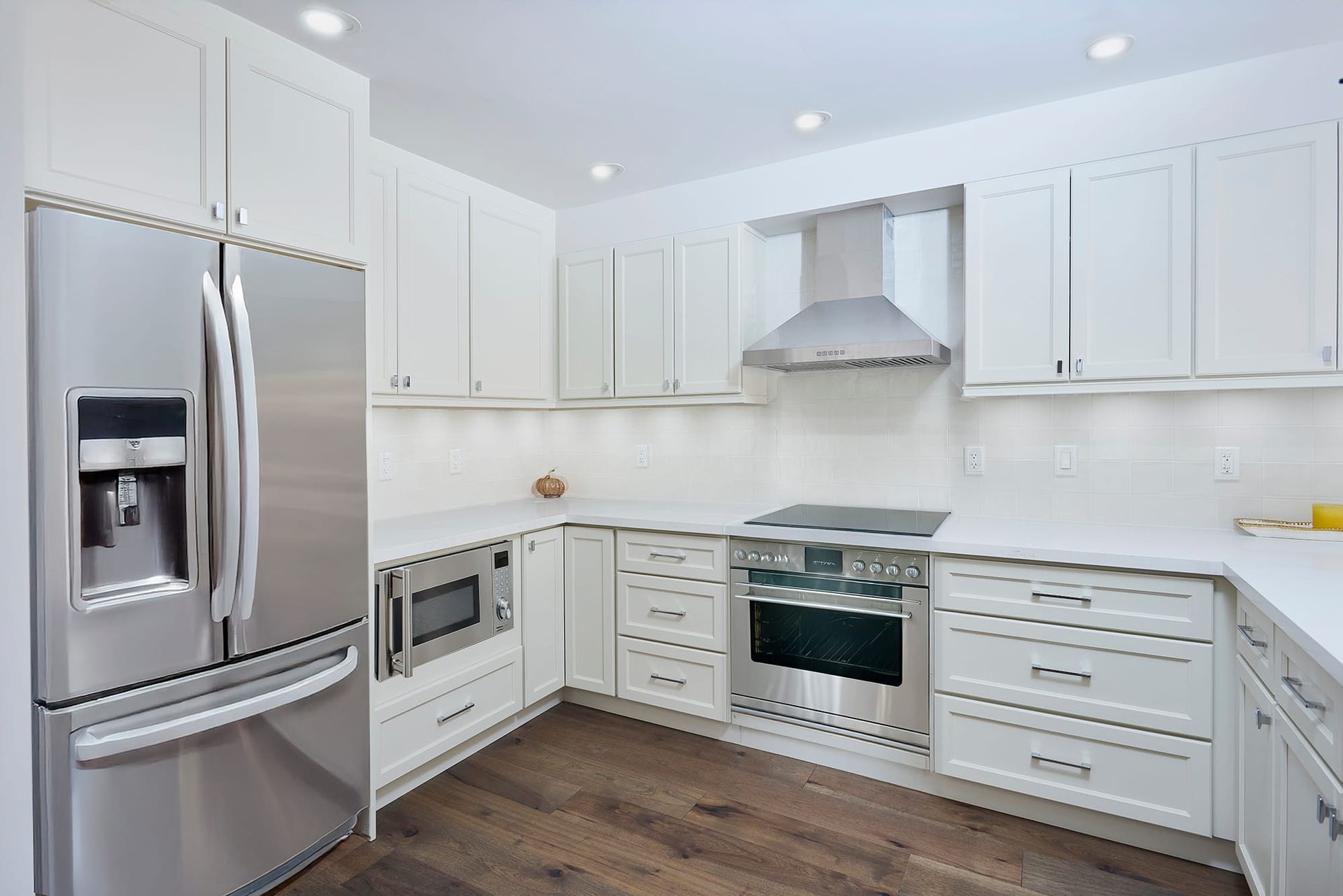 White kitchen with stainless steel appliances and wood floor.