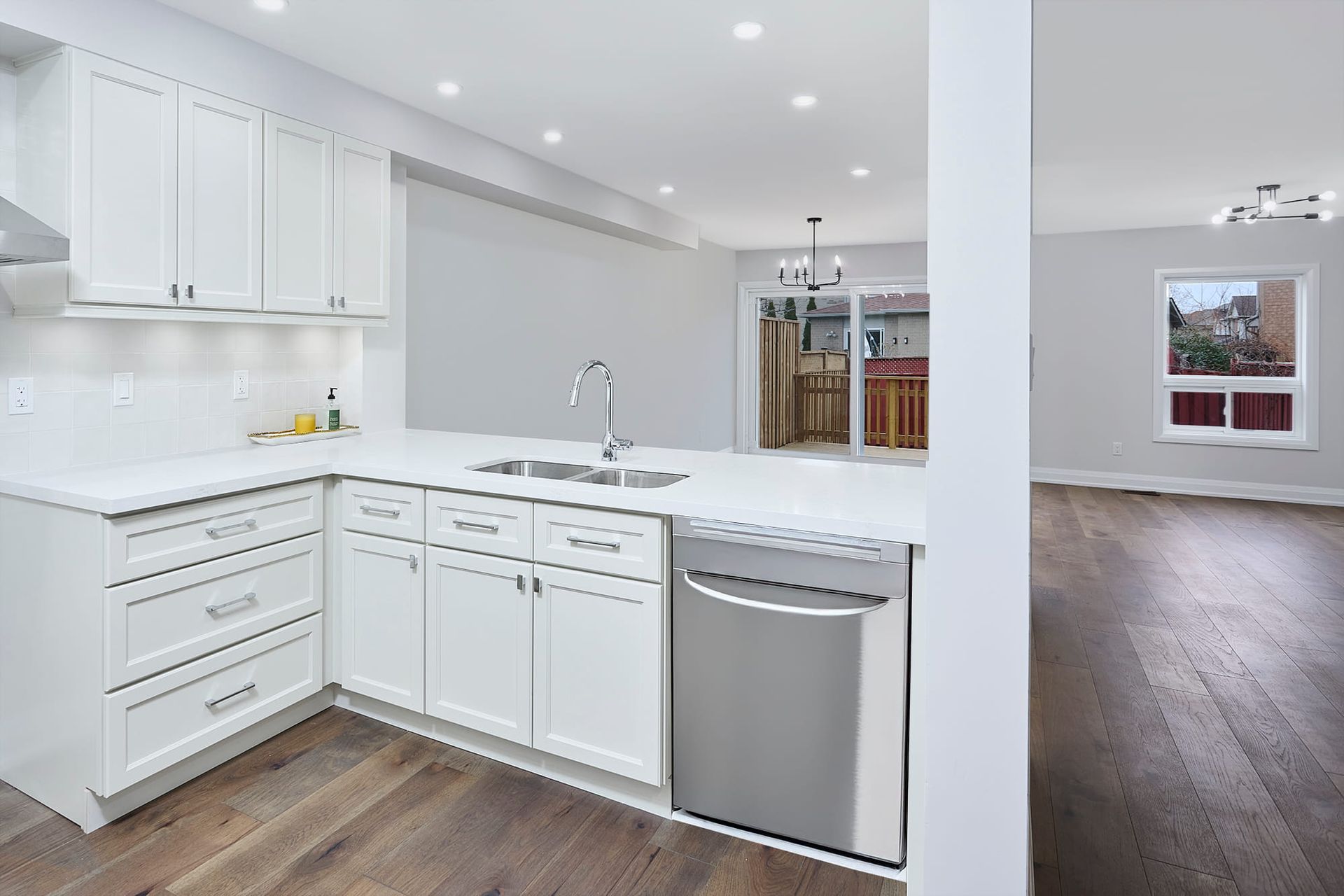 White kitchen with stainless steel appliances, open to a dining and living area.